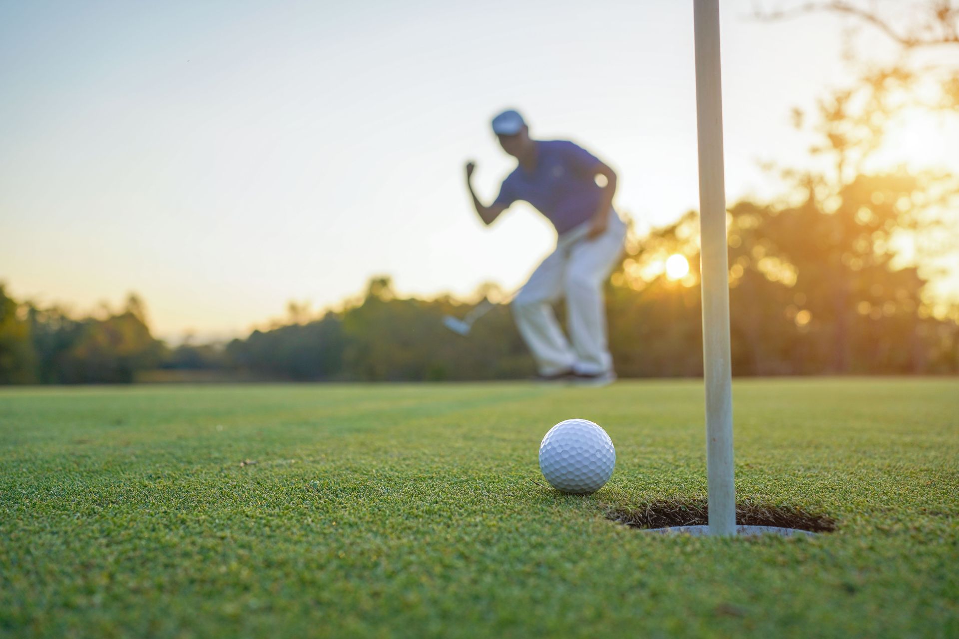 A man is putting a golf ball into a hole on a golf course.