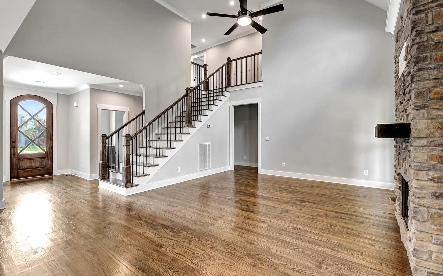 Open-concept home interior with wooden floors, staircase, and stone fireplace.