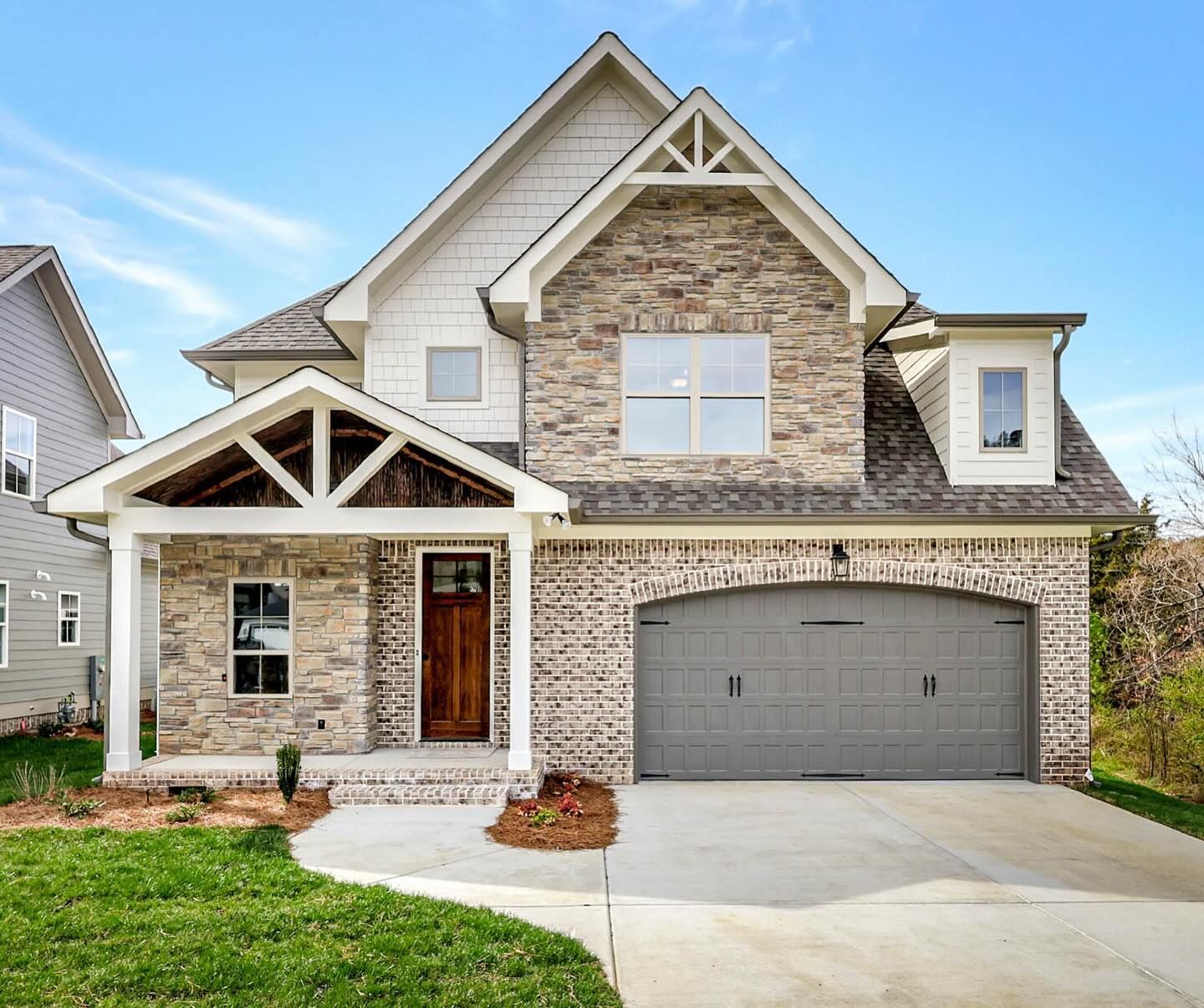 Two-story house with brick and siding exterior, arched garage door, and covered front porch on a sunny day.