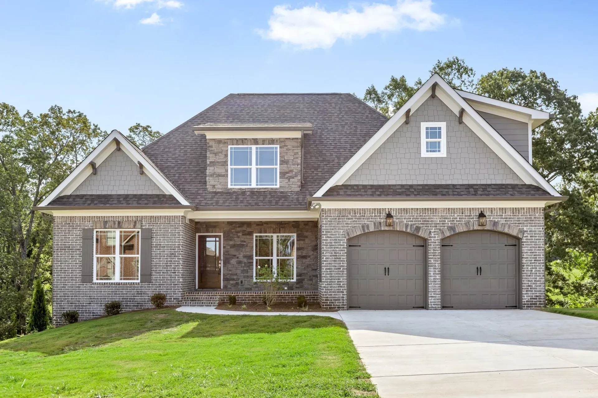 Brick home with a gray roof and two-car garage, set on a green lawn.