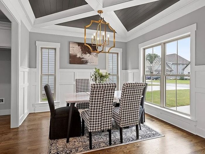 Dining room with gray walls, wooden floor, patterned chairs, and a gold chandelier.