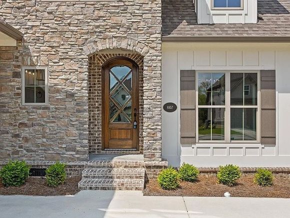 Stone and white brick house facade with arched wooden door and brown shutters.