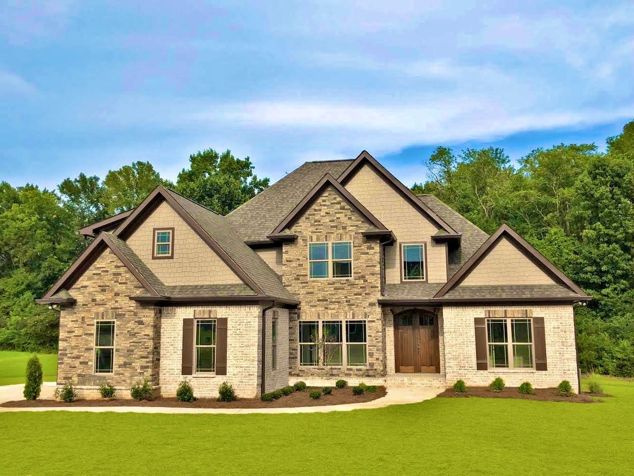 Stone and tan house with multiple windows, brown shutters, and green lawn.