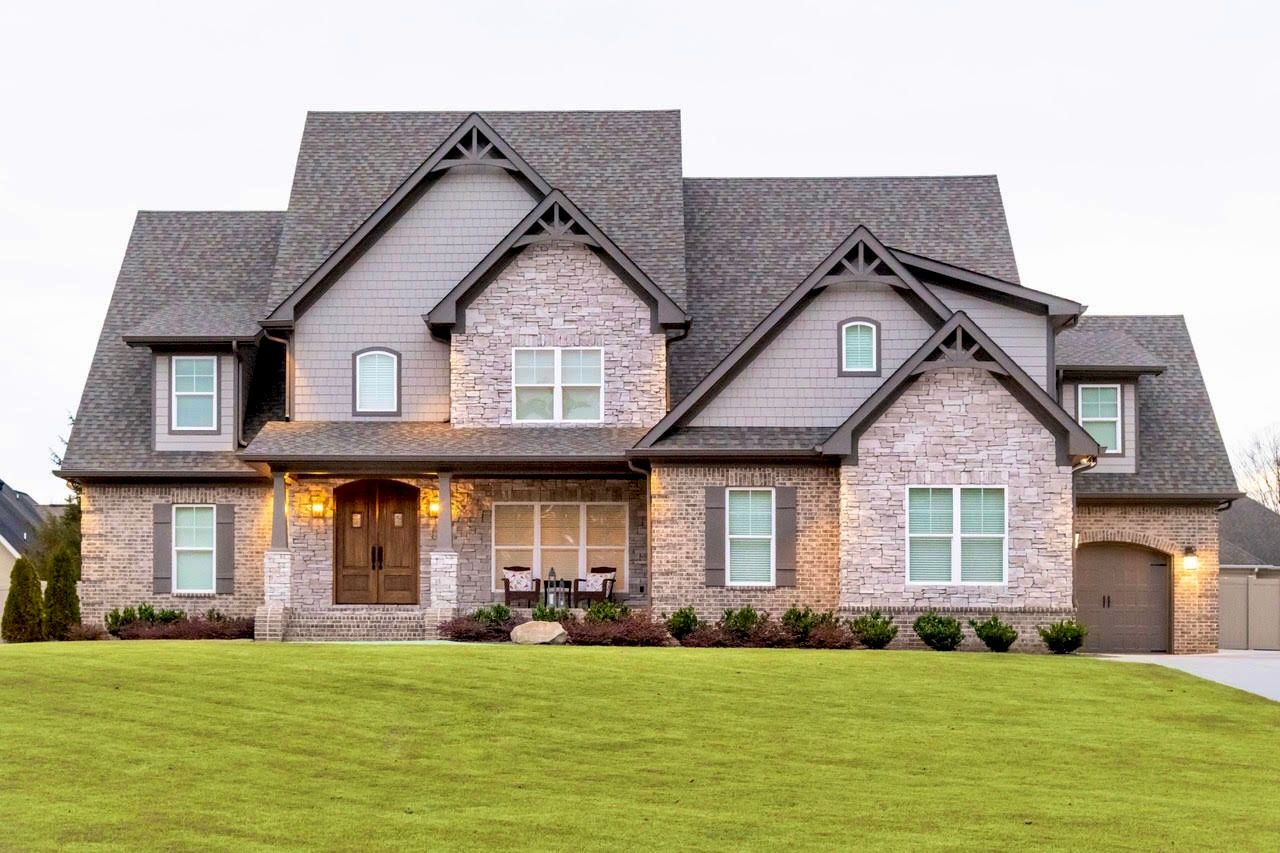 Two-story house with brick and gray siding, green lawn, and a light-colored sky.