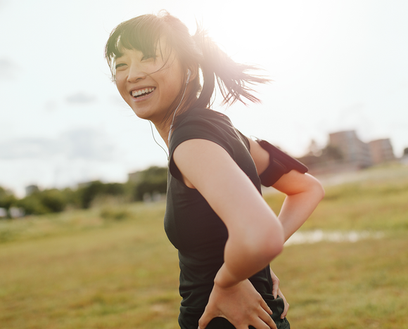 A woman is standing in a field with her hands on her hips and smiling.