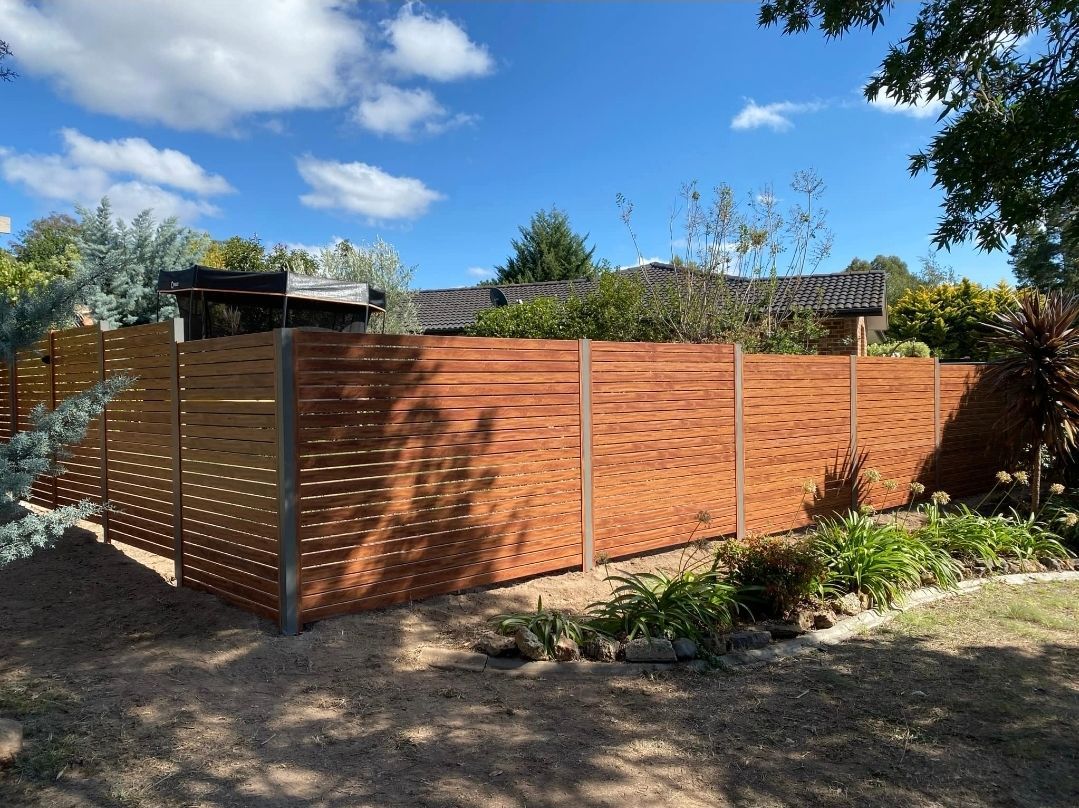 Wooden slat fence enclosing a garden under a bright blue sky with scattered clouds. — GnB Fencing and Excavation in Queanbeyan, NSW
