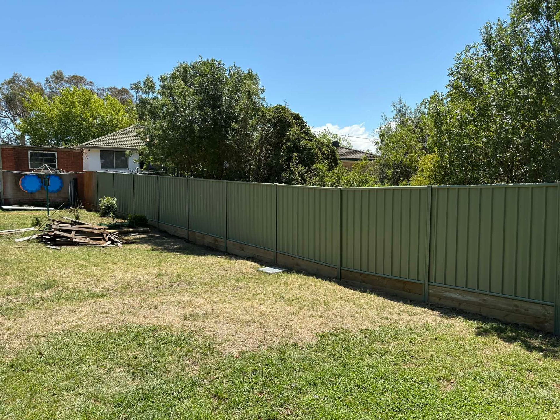 Backyard with a green fence, grassy lawn, trees, and a small shed under a clear blue sky — GnB Fencing and Excavation in Queanbeyan, NSW