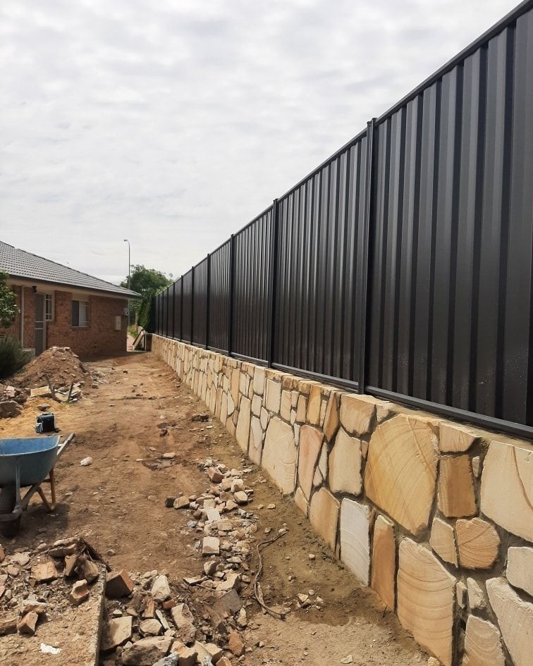 A Stone Wall Is Being Built Next to A Metal Fence  — GnB Fencing and Excavation in Queanbeyan, NSW
