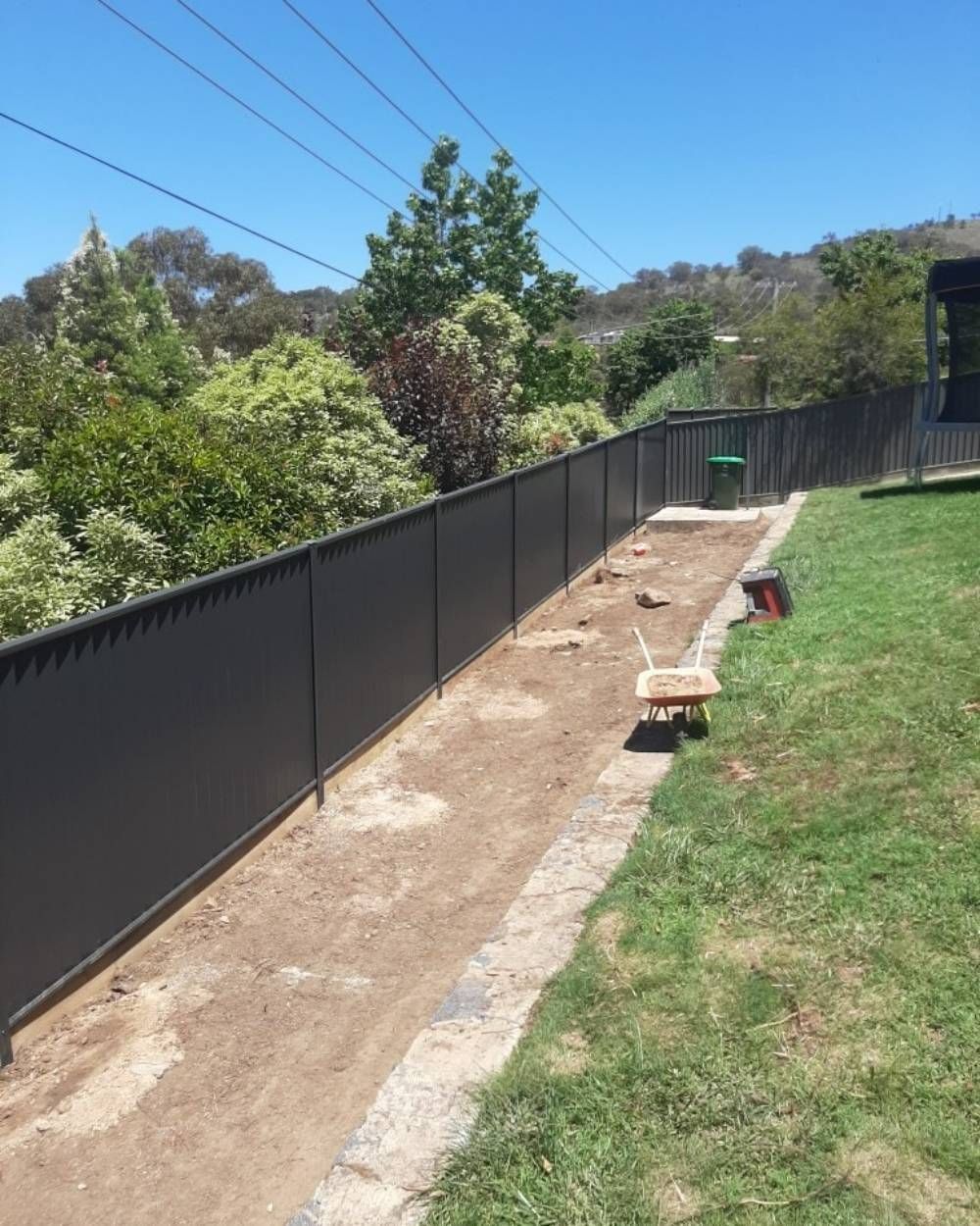 A Black Fence Surrounds a Lush Green Yard  — GnB Fencing and Excavation in Queanbeyan, NSW