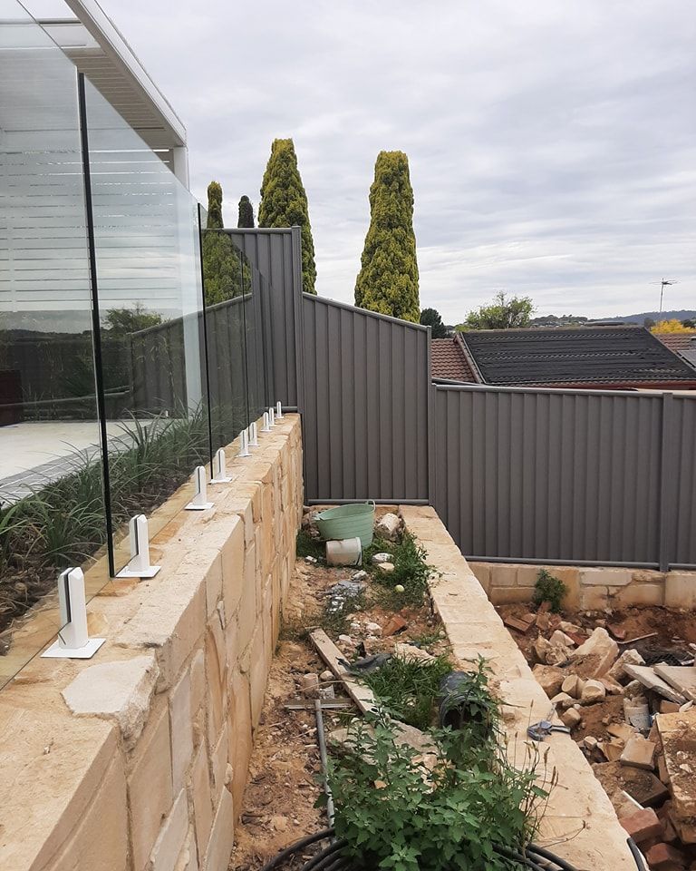 A Fence Is Being Built Next to A Stone Wall — GnB Fencing and Excavation in Queanbeyan, NSW