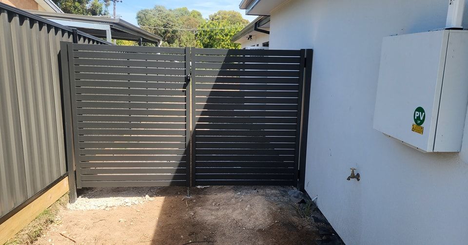 A Black Fence Is Sitting Next to A White House — GnB Fencing and Excavation in Queanbeyan, NSW