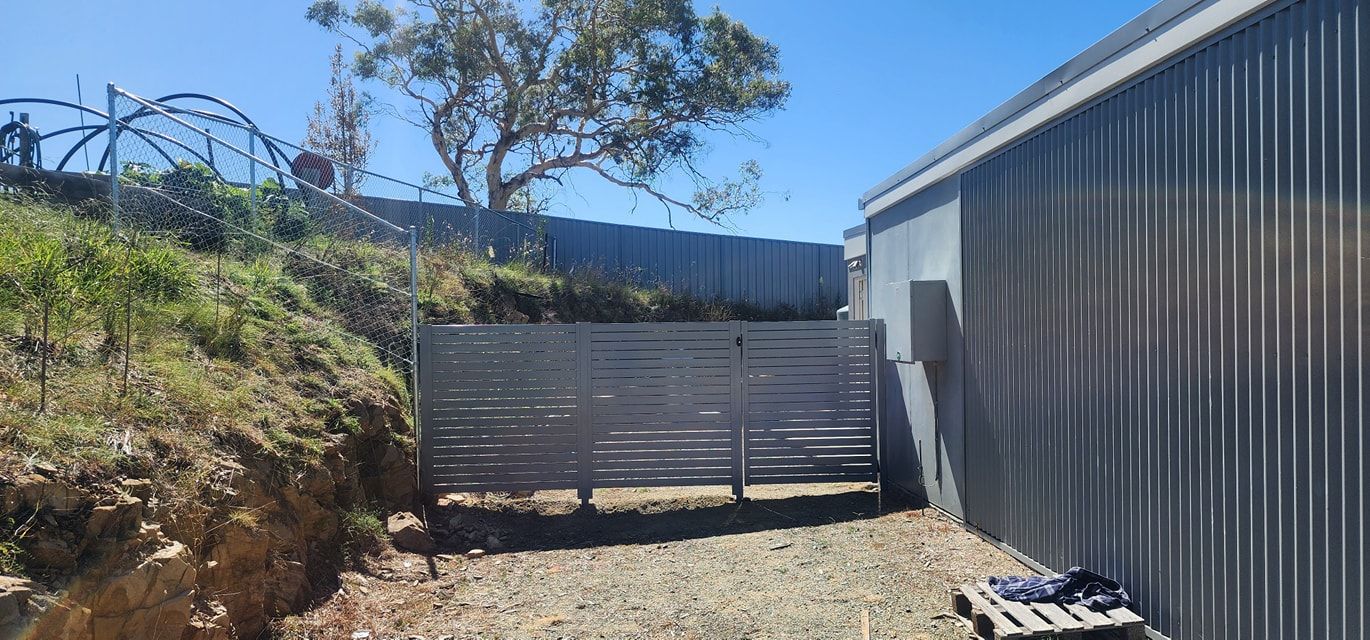 A Metal Building with A Wooden Fence in Front of It  — GnB Fencing and Excavation in Queanbeyan, NSW