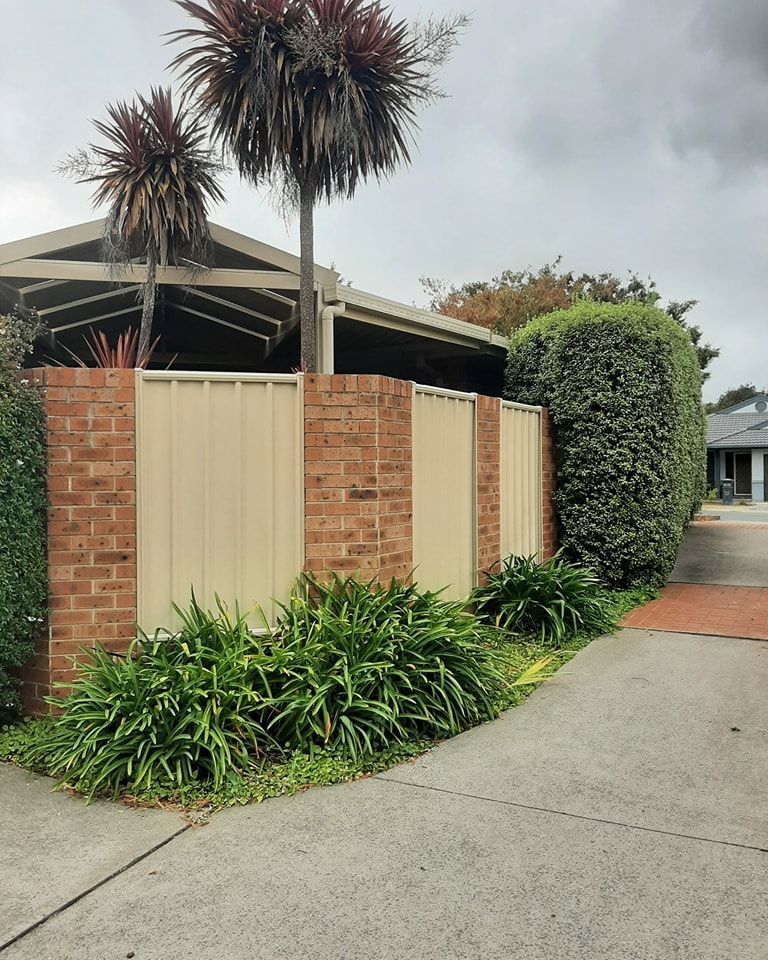 A Brick Fence Surrounds a House with Palm Trees in The Background  — GnB Fencing and Excavation in Queanbeyan, NSW