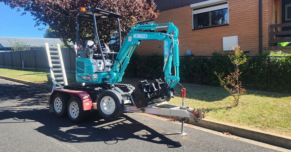 A Blue Excavator Is Parked on The Side of The Road Next to A Trailer  — GnB Fencing and Excavation in 
Queanbeyan, NSW