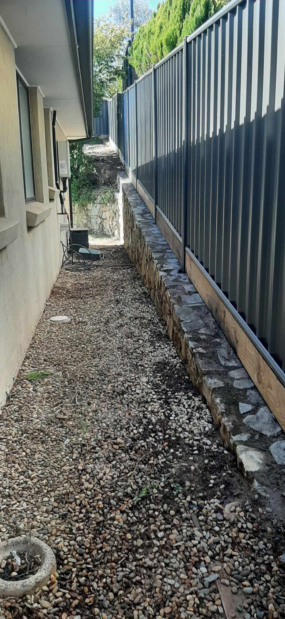 Narrow gravel side yard beside a house and dark fence, with a small plant at the end. — GnB Fencing and Excavation in Queanbeyan, NSW