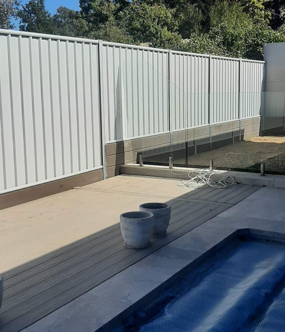 Backyard patio with a blue pool, white fence, and two buckets on a wooden deck — GnB Fencing and Excavation in Queanbeyan, NSW
