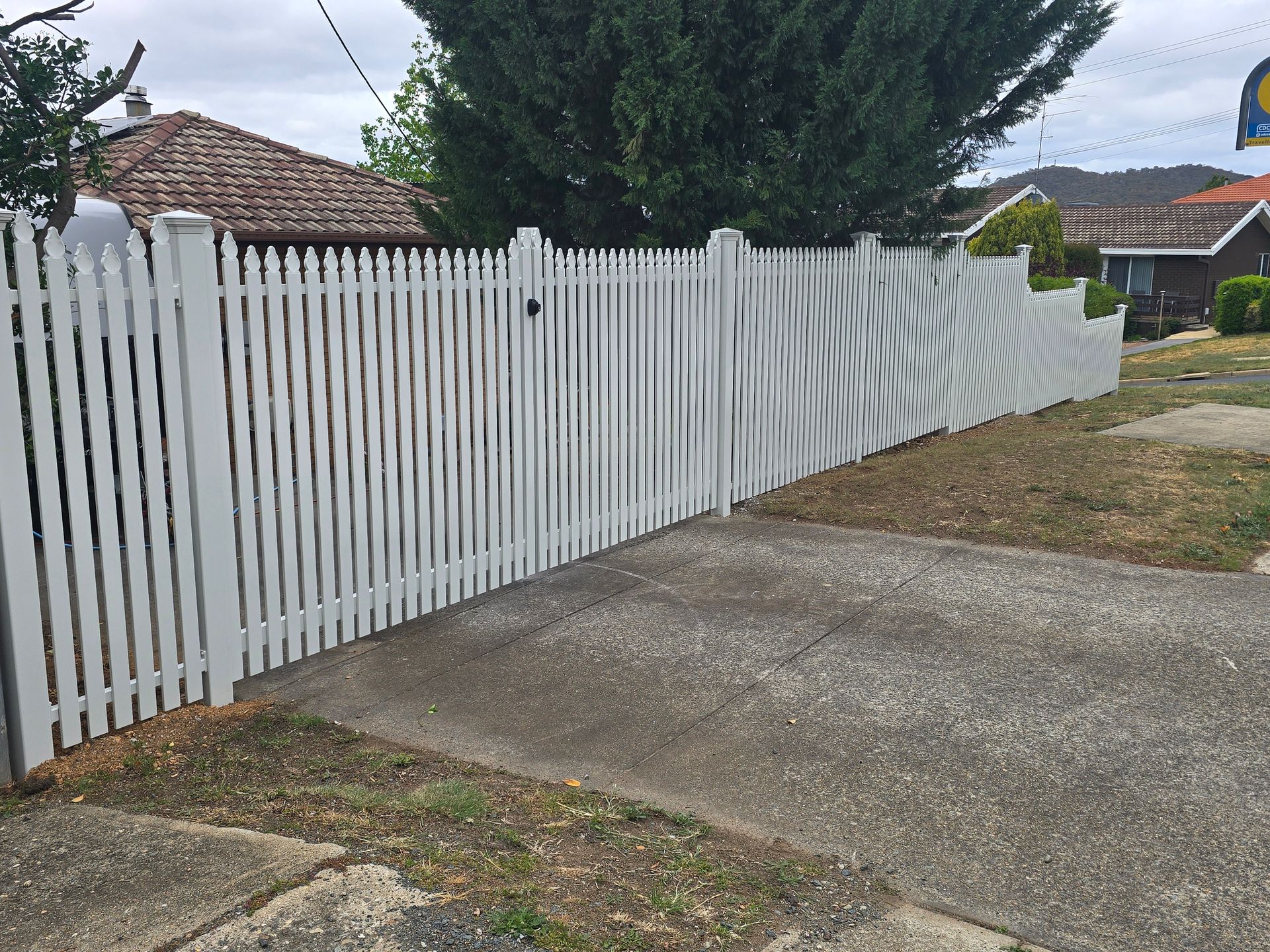 White picket fence beside a concrete driveway, with a draped gray tarp and suburban houses in the background — GnB Fencing and Excavation in Queanbeyan, NSW