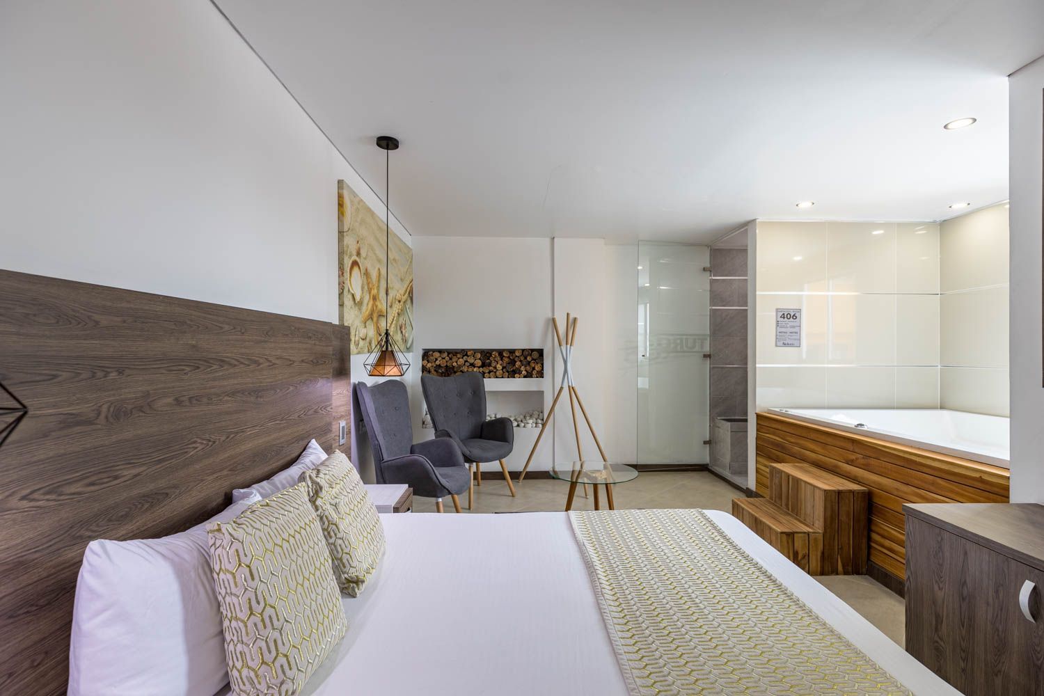 Una habitación de hotel con una cama, dos sillones y jacuzzi. La decoración es moderna, con tonos neutros y detalles en madera.