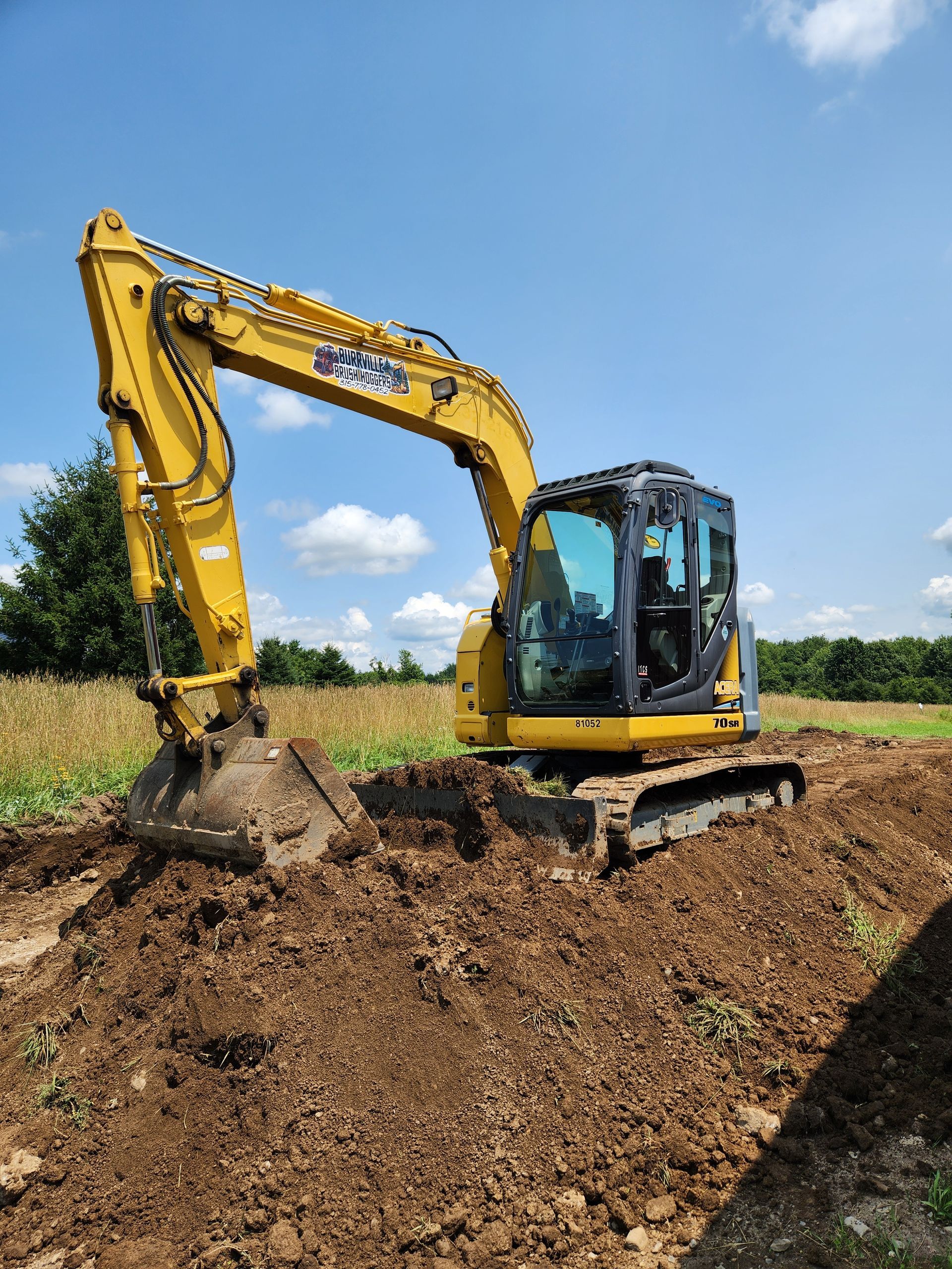 Yellow excavator digging soil in a field under a blue sky