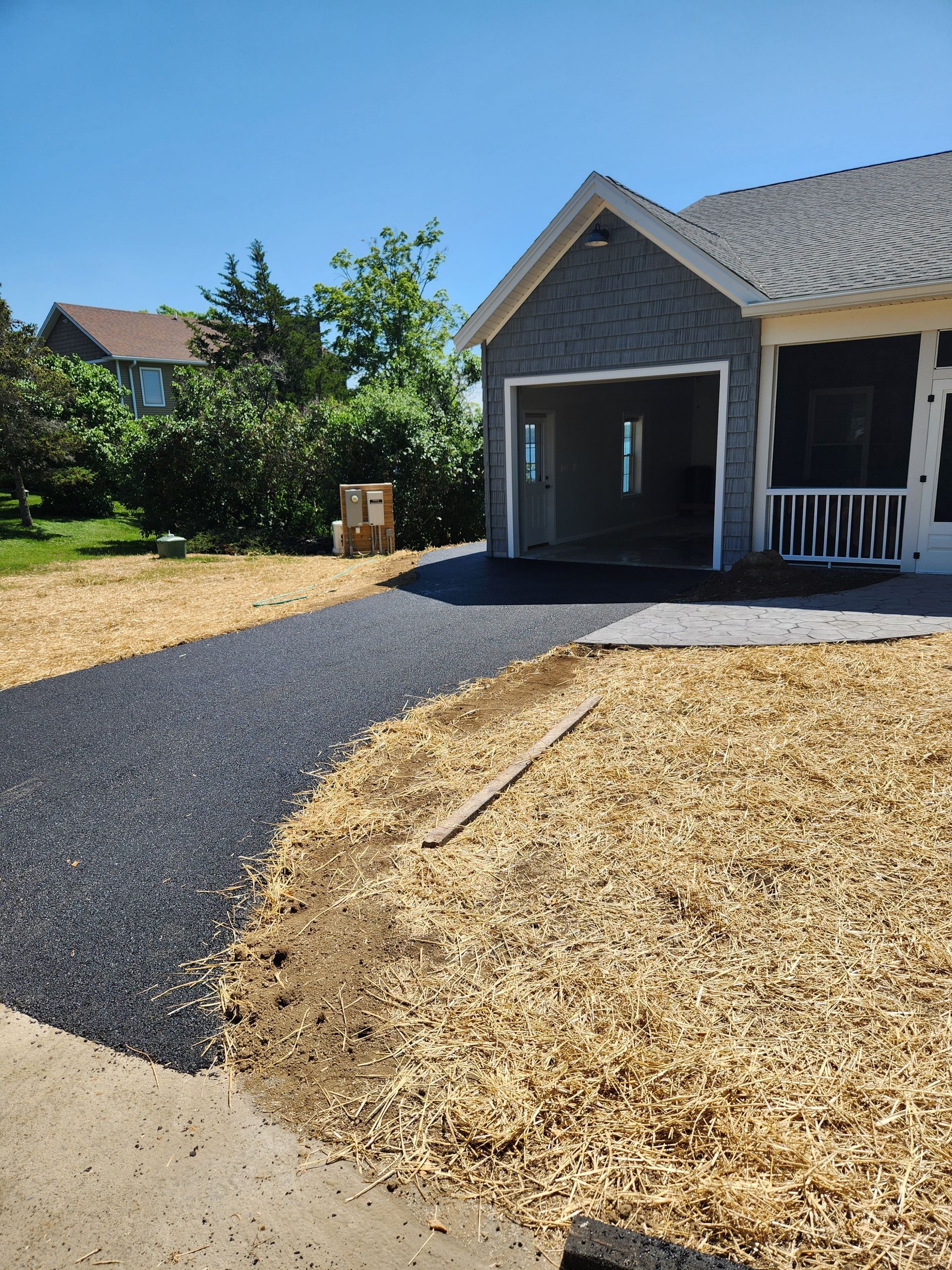Front yard with new dark gravel driveway, tan mulch beds, and a gray house with a covered porch.