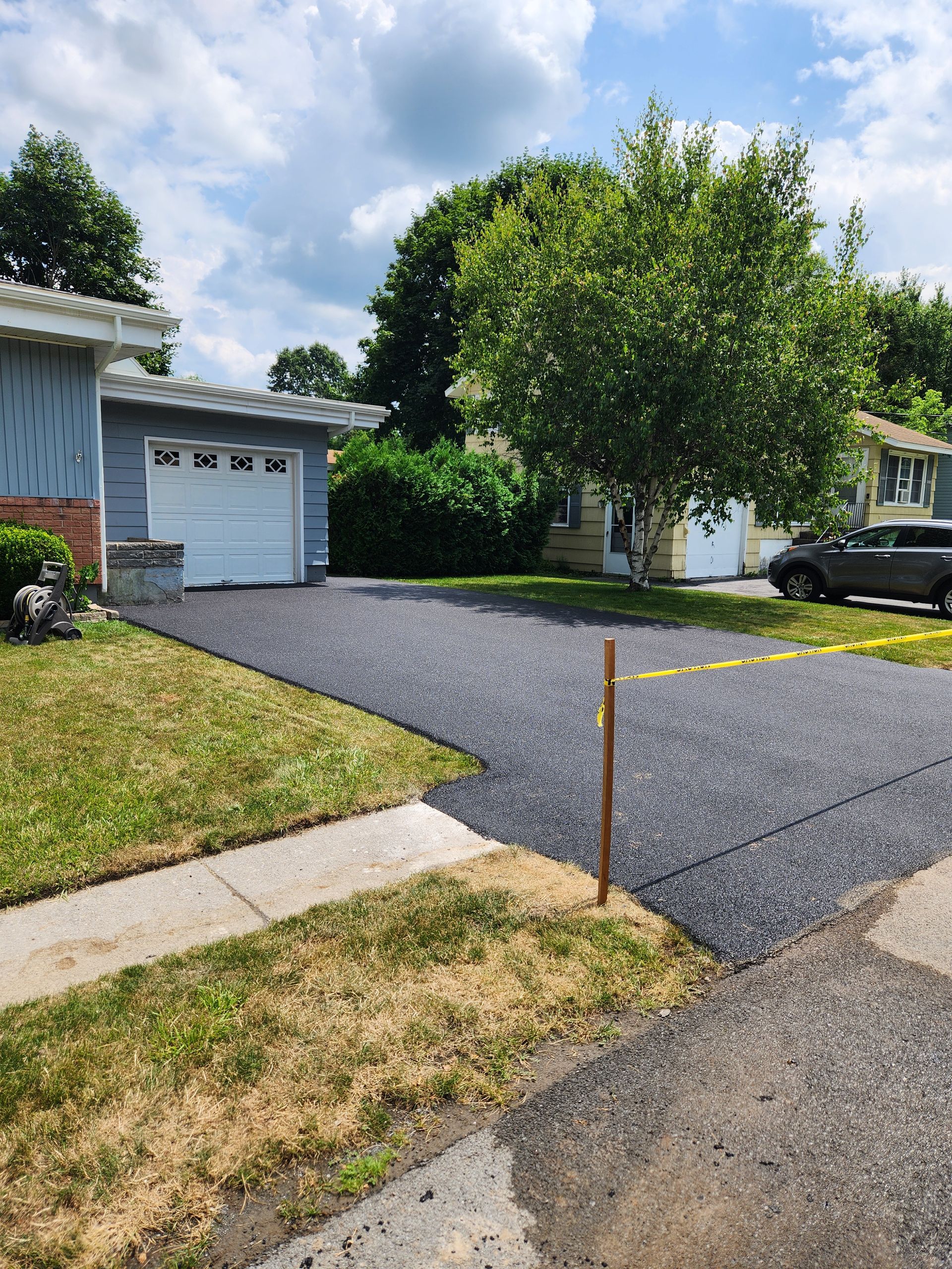 Suburban house with a new black asphalt driveway, garage, front lawn, and a parked pickup truck.