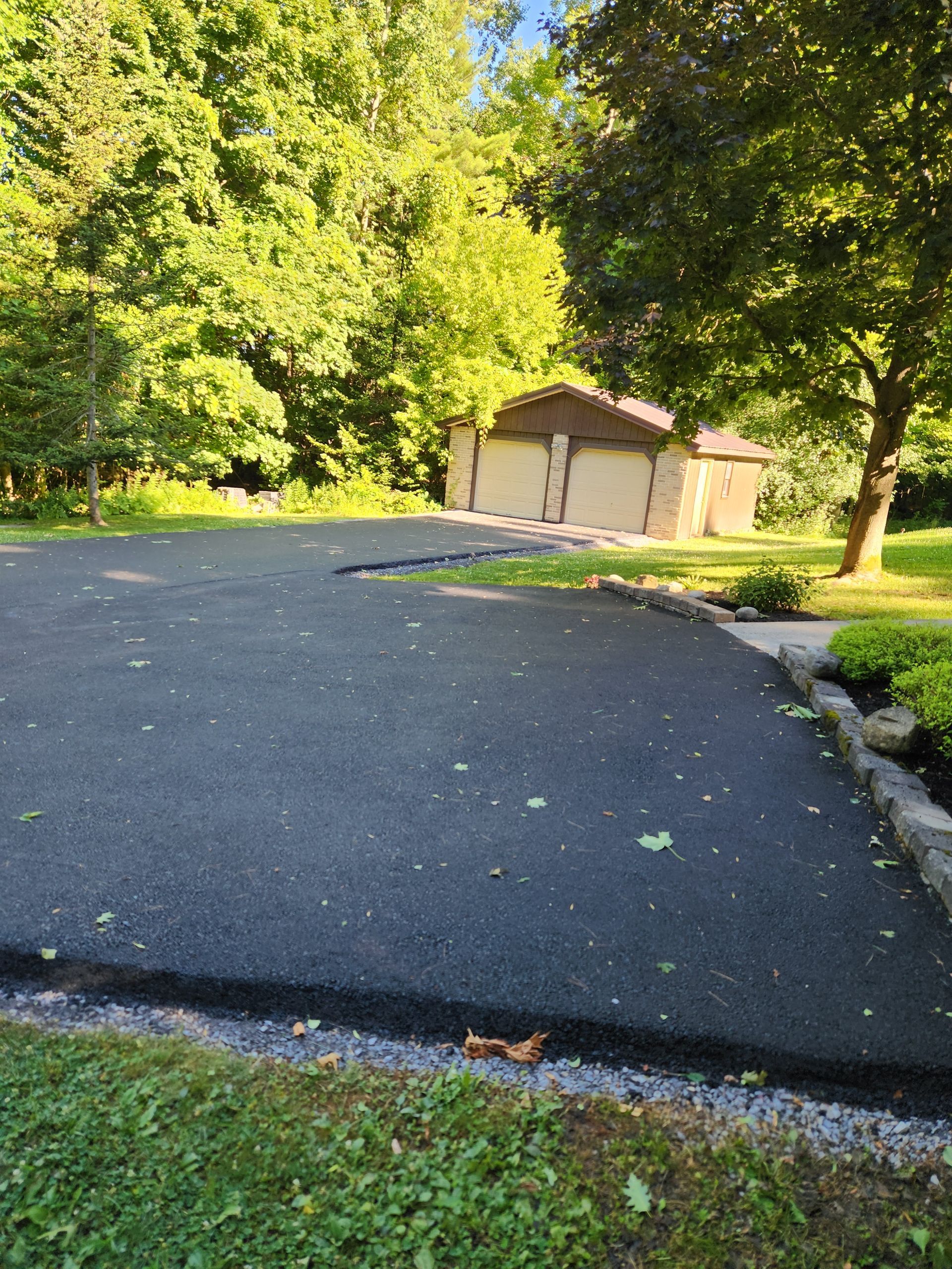 Paved driveway beside green trees, leading to a small shed in the background.
