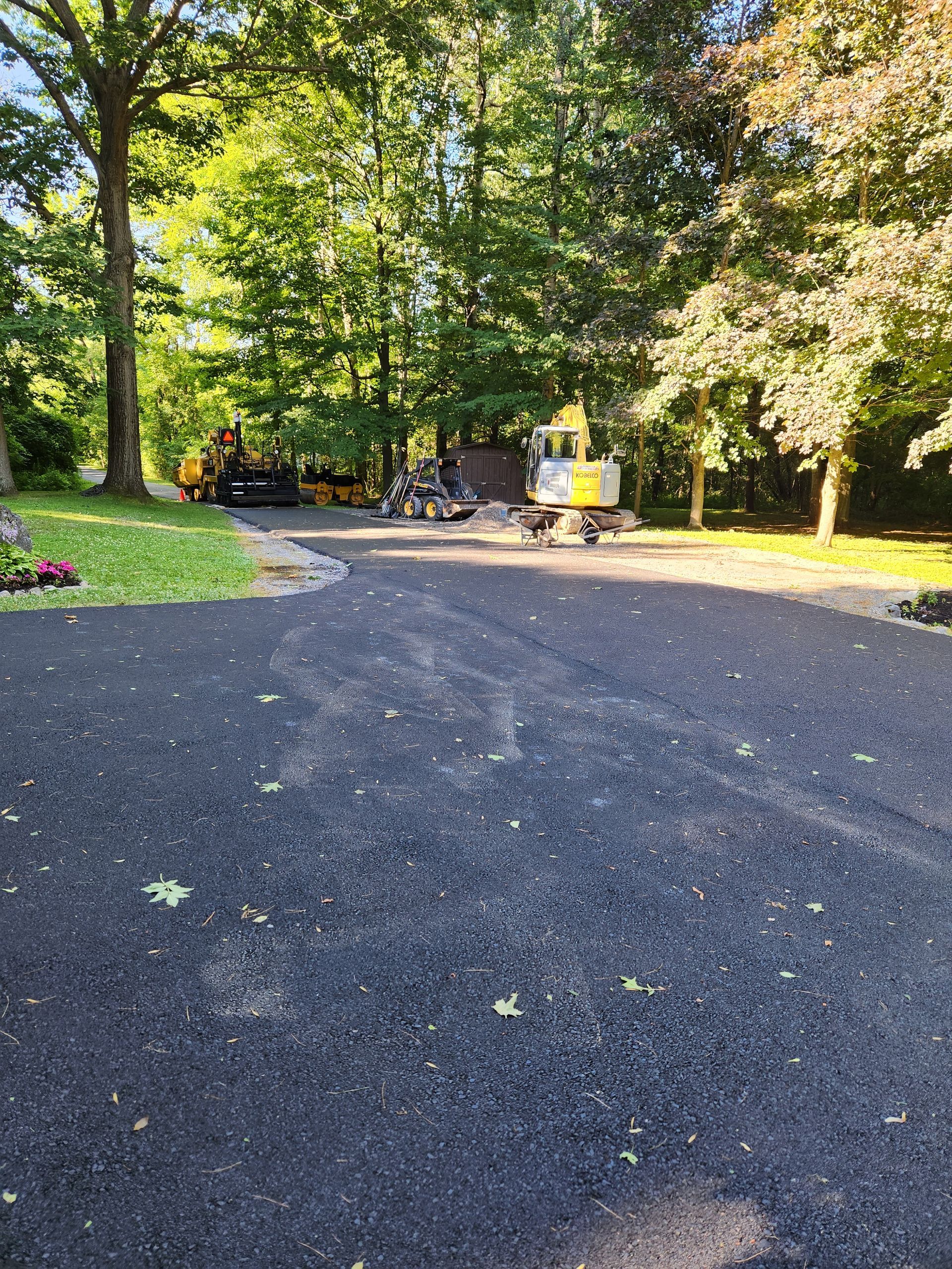 Gravel path in a sunlit park with trees, flowers, and a few people near the benches.