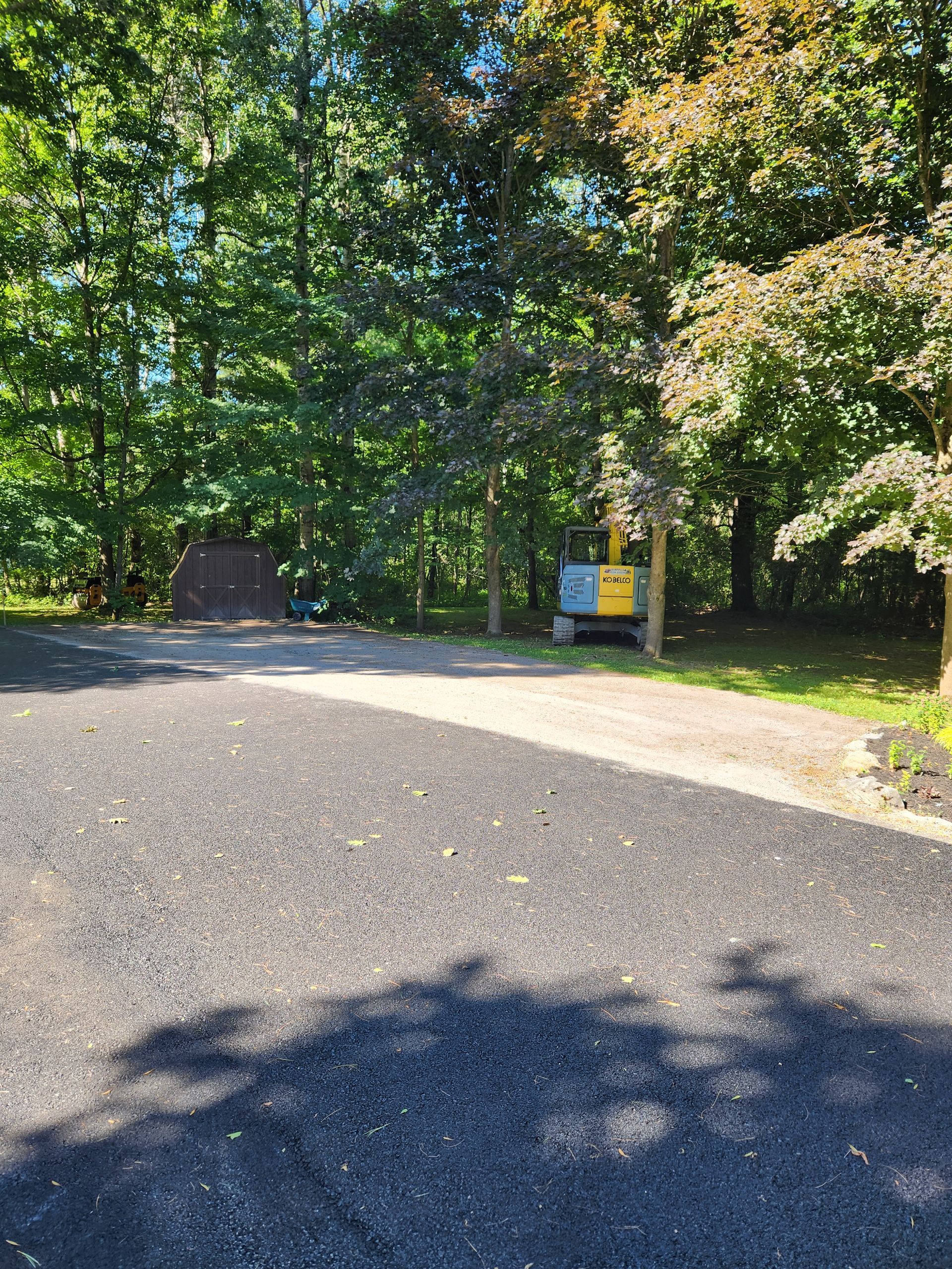 Gravel path leading into a wooded park with a sign and shaded trees on a sunny day