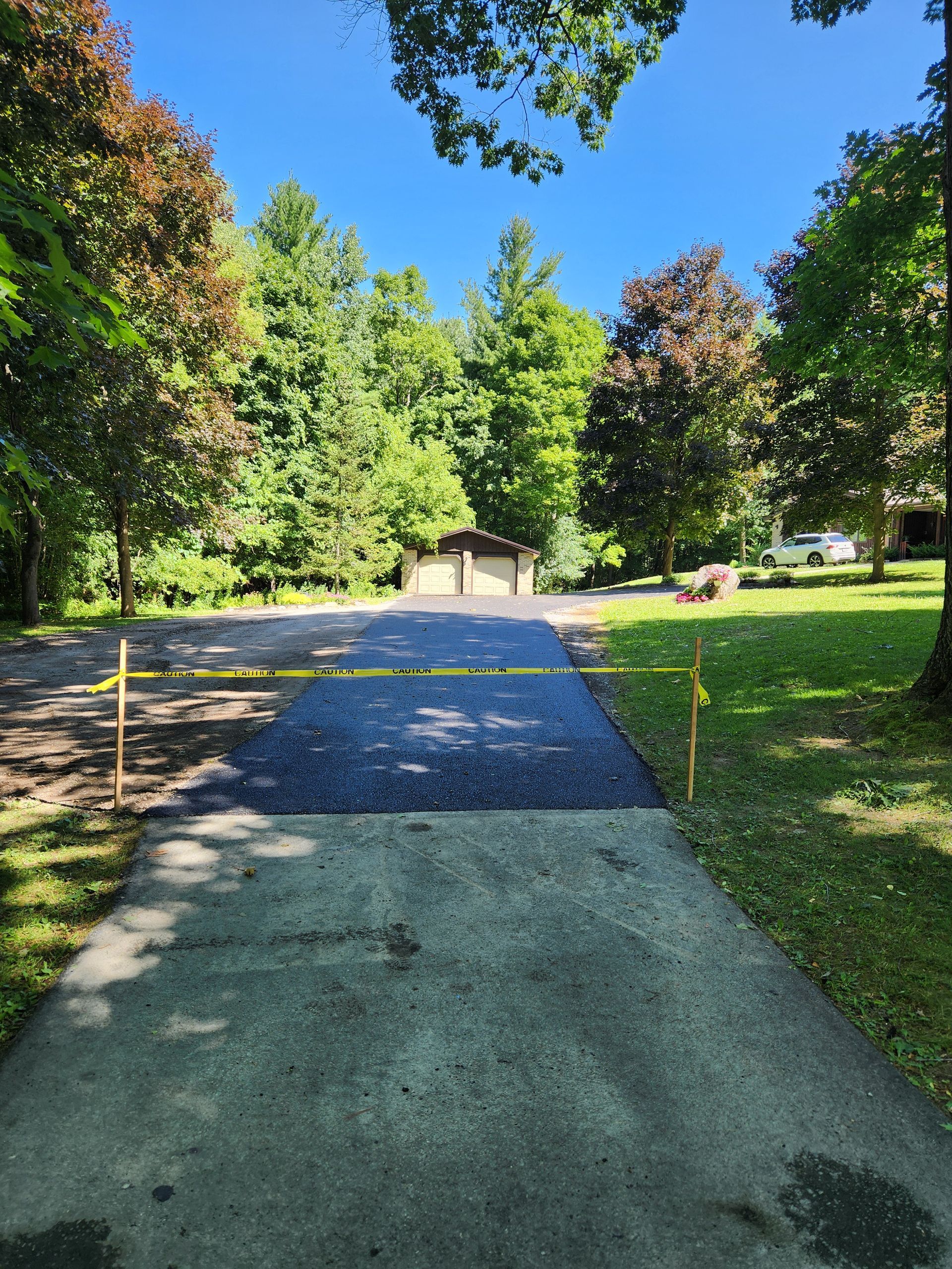 Gravel park path bordered by grass and trees, leading toward a small building under a blue sky