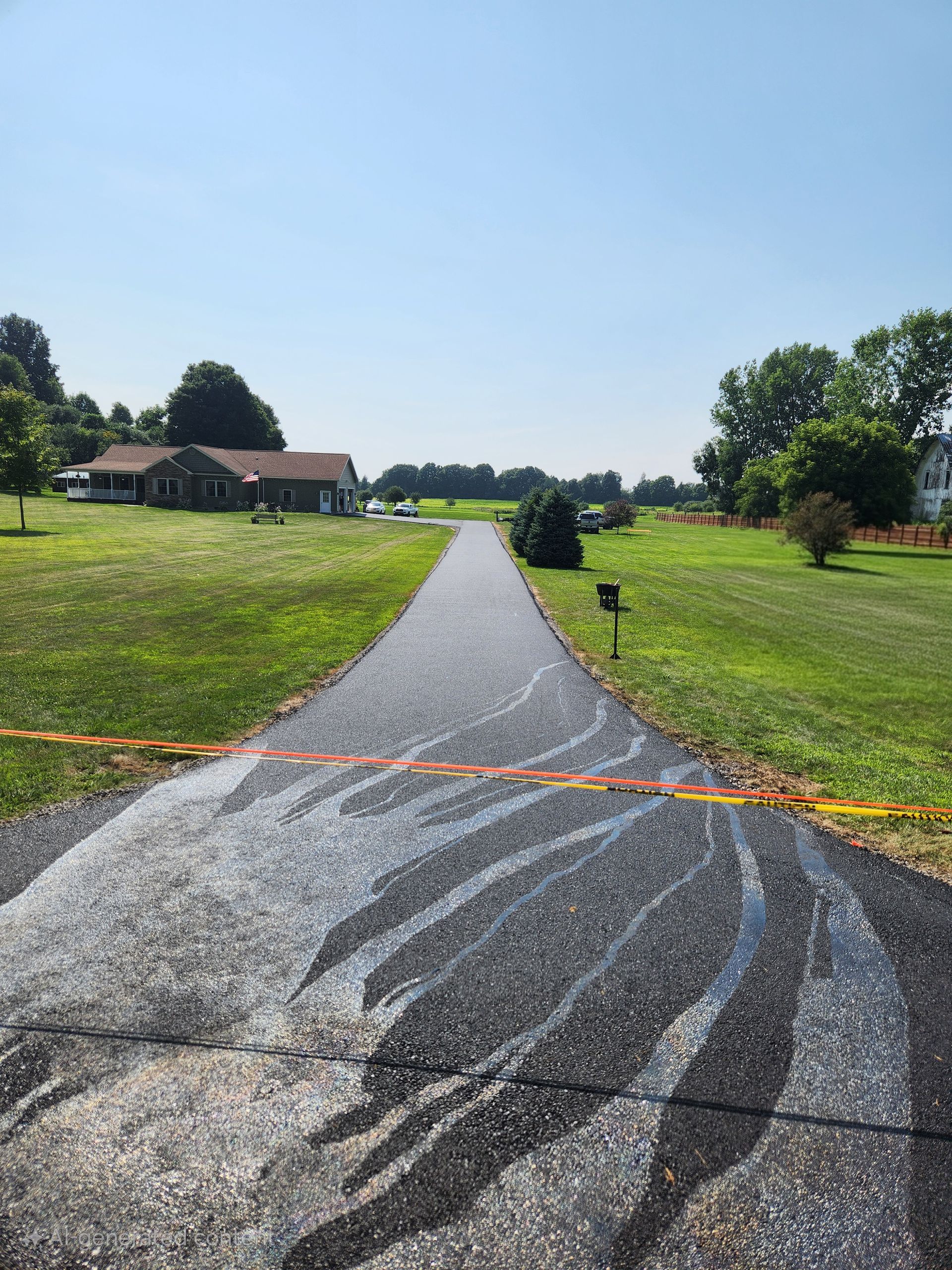 Gravel path through a sunny green field toward houses, with orange tape blocking the entrance