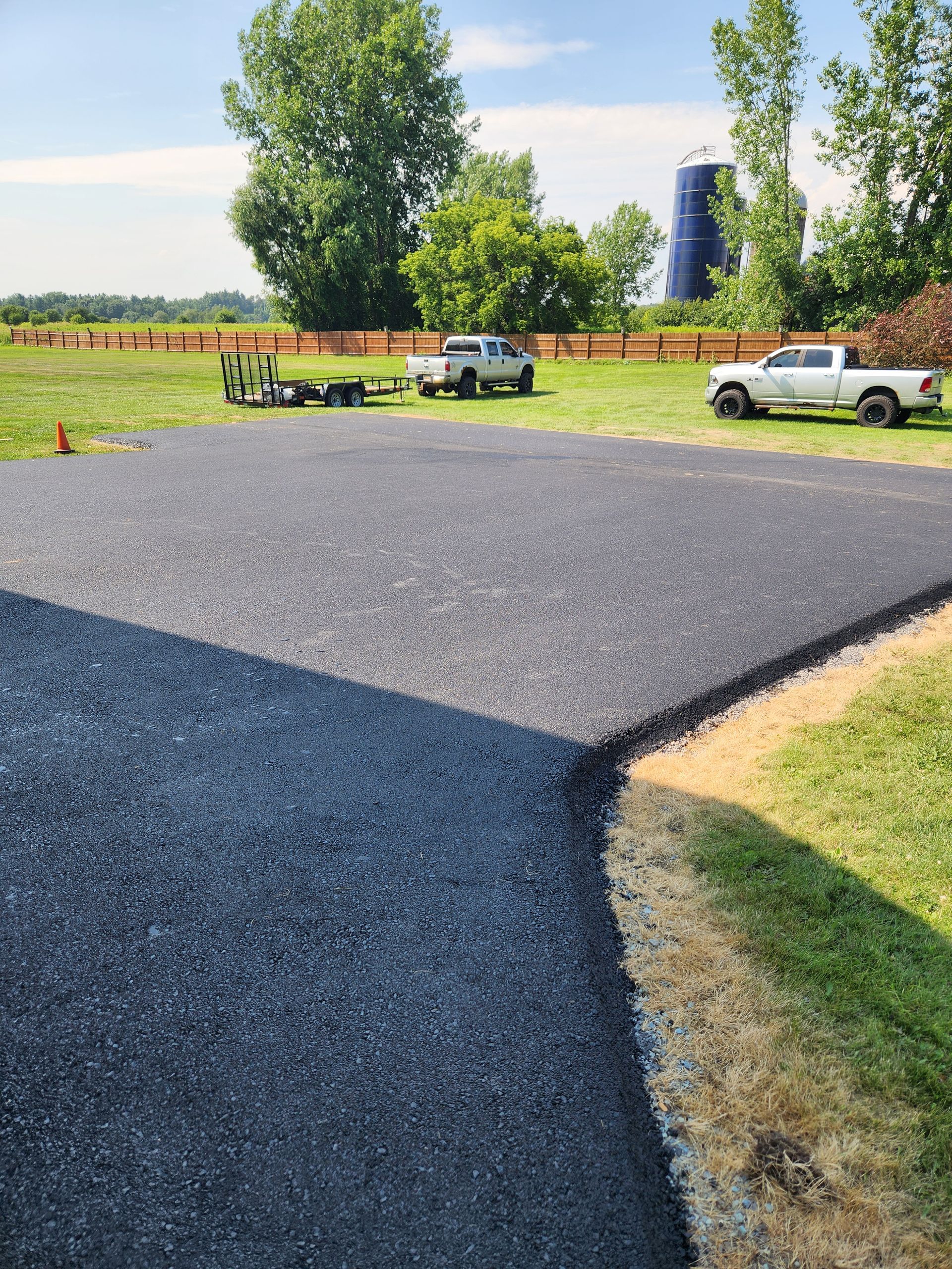Freshly paved driveway with parked pickup trucks and trees in the background