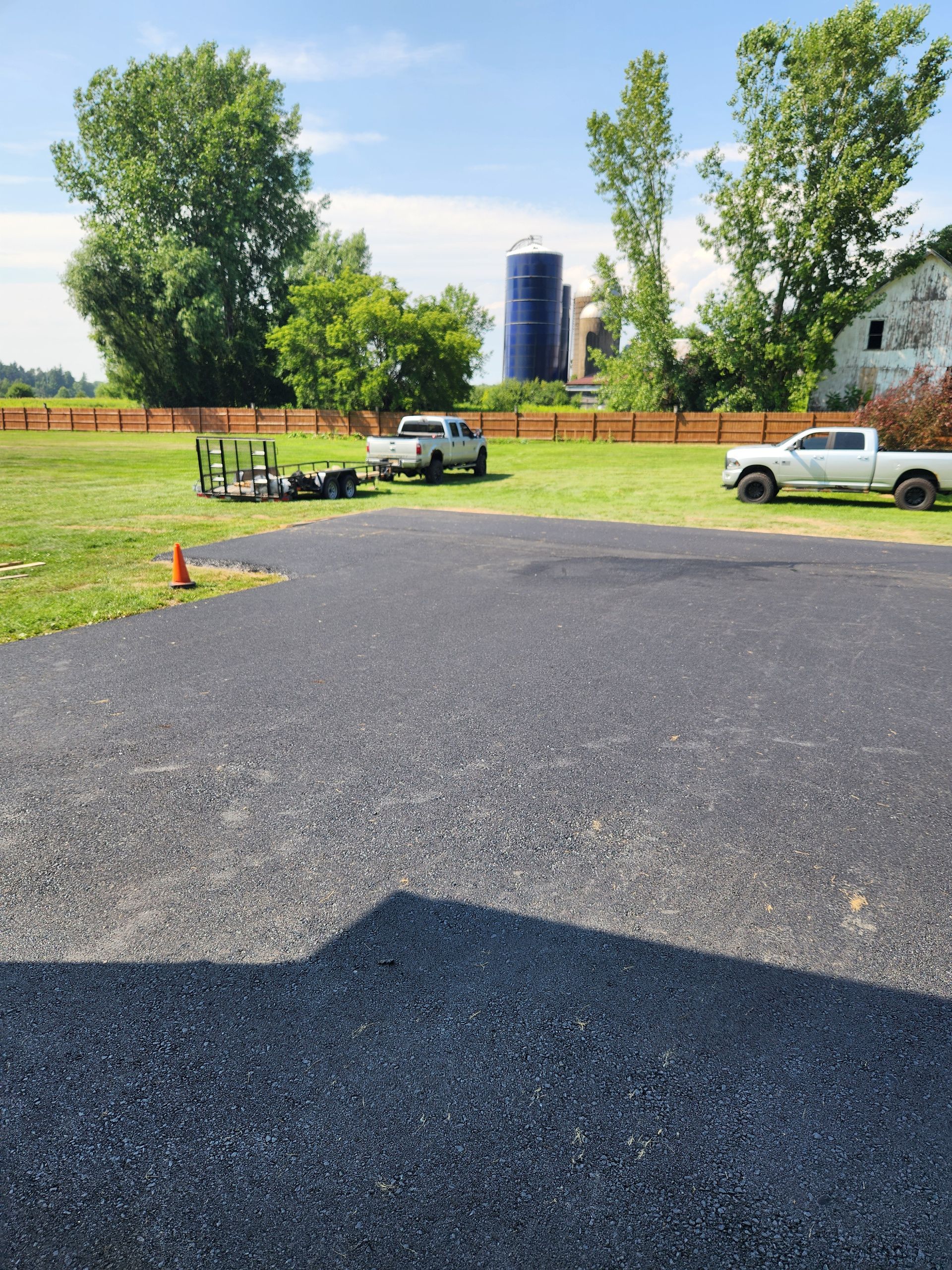 Gravel lot with parked white trucks, green trees, and a blue silo under a clear sky