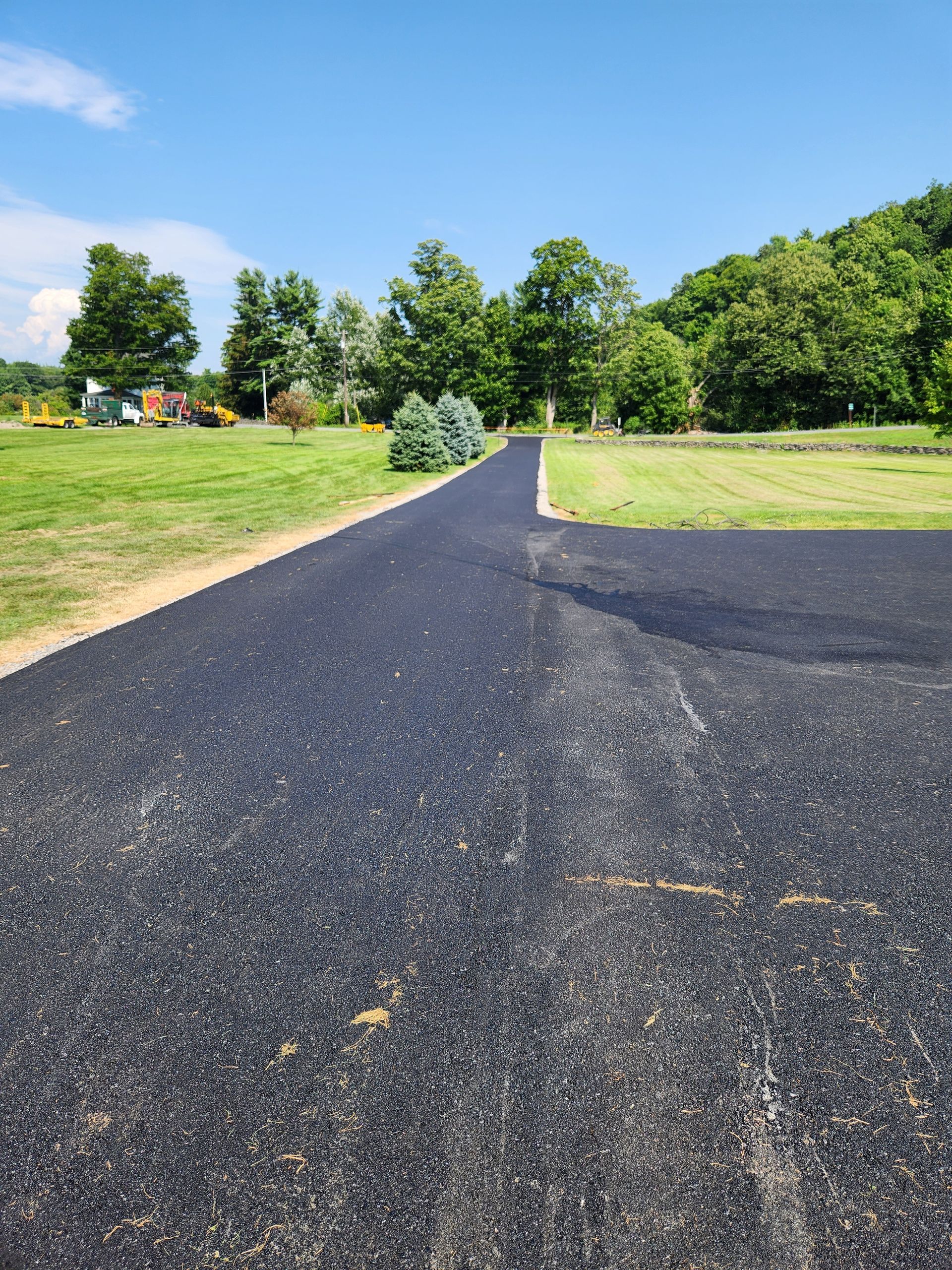 Fresh blacktop path through a green park with trees and grassy fields under a blue sky