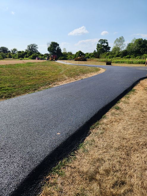 Curving black gravel path through grassy park under a blue sky