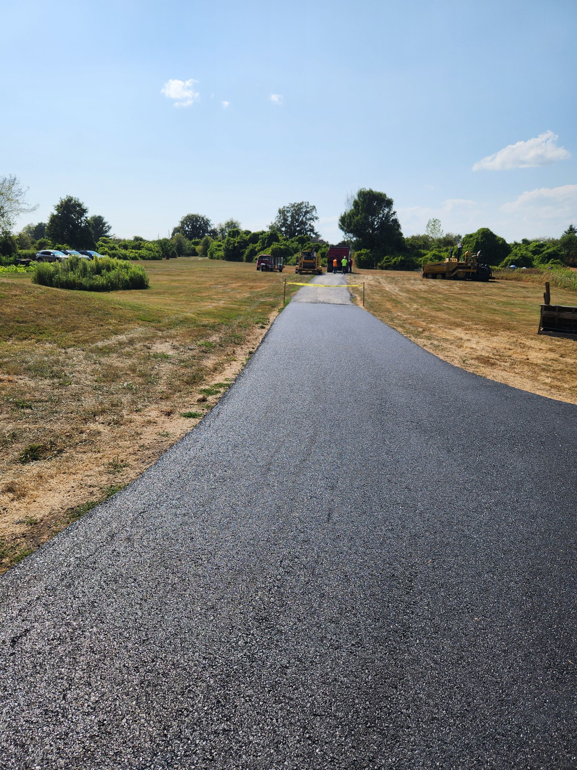Gravel path through a sunny landscaped park with flowerbeds and trees under a blue sky