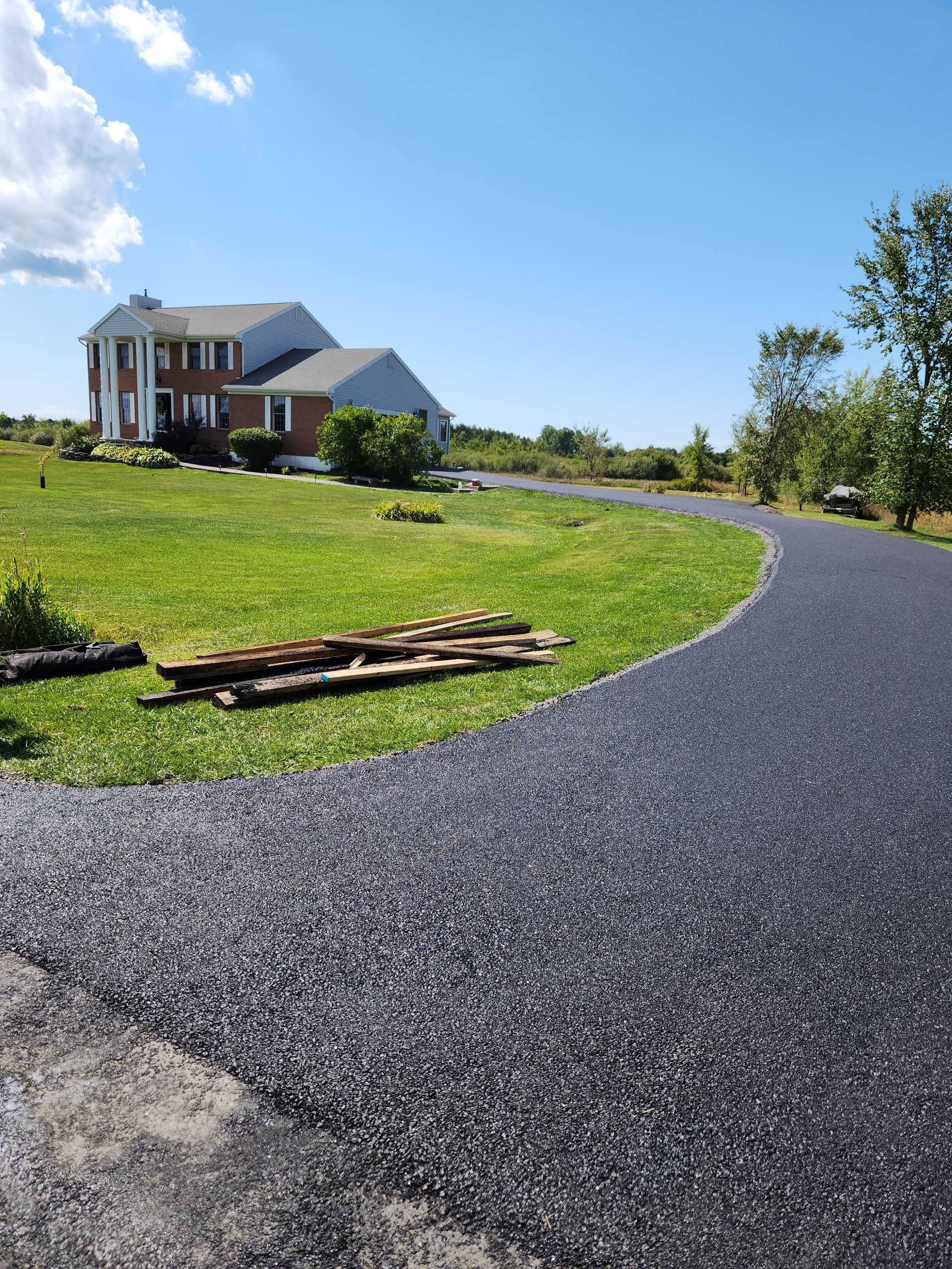 Gravel driveway curving through a green lawn toward a brick house under a blue sky
