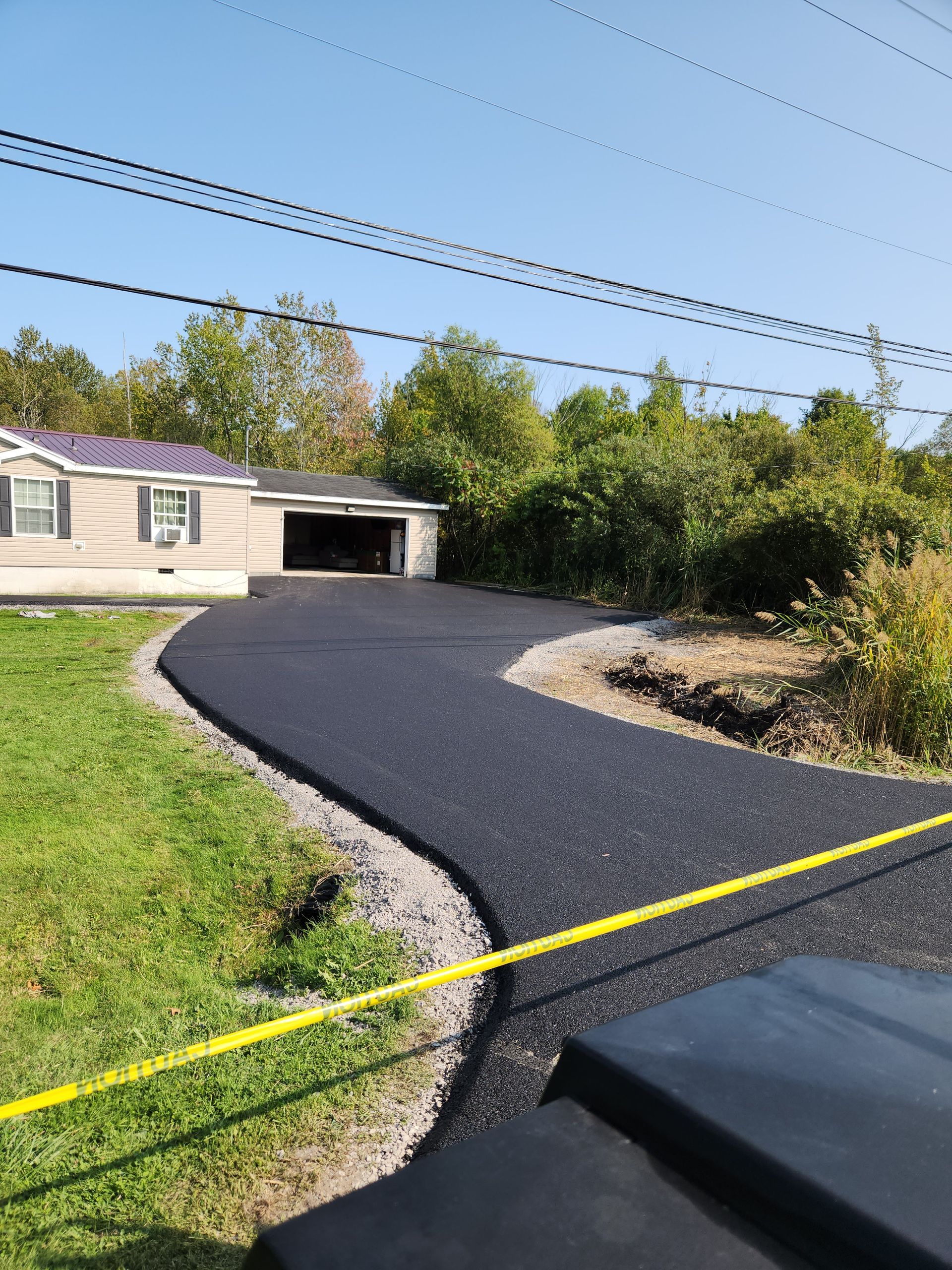 Freshly paved black driveway curving to a house garage with yellow caution tape across the foreground