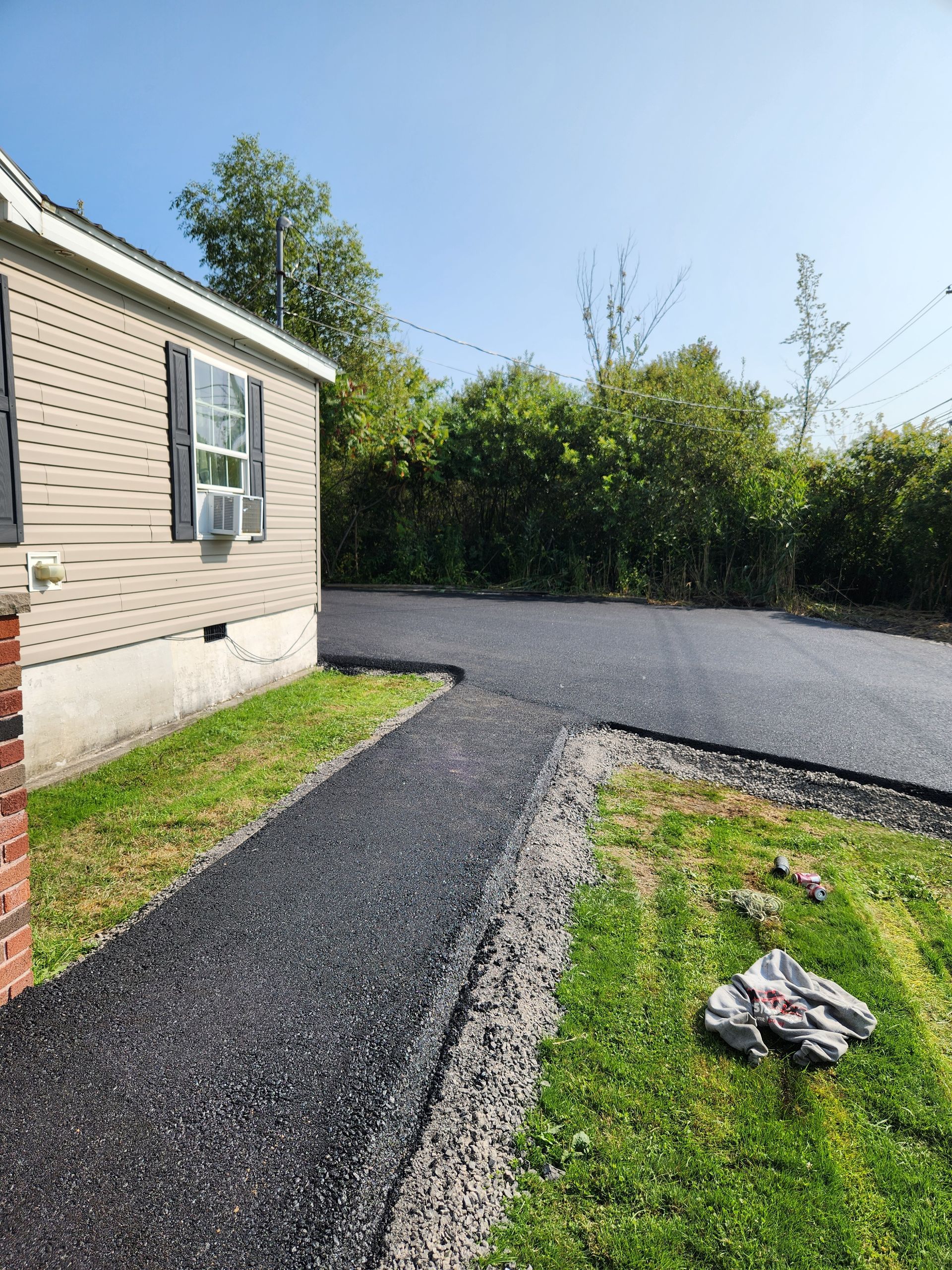 Gravel driveway beside a beige house, bordered by green grass and hedges on a sunny day