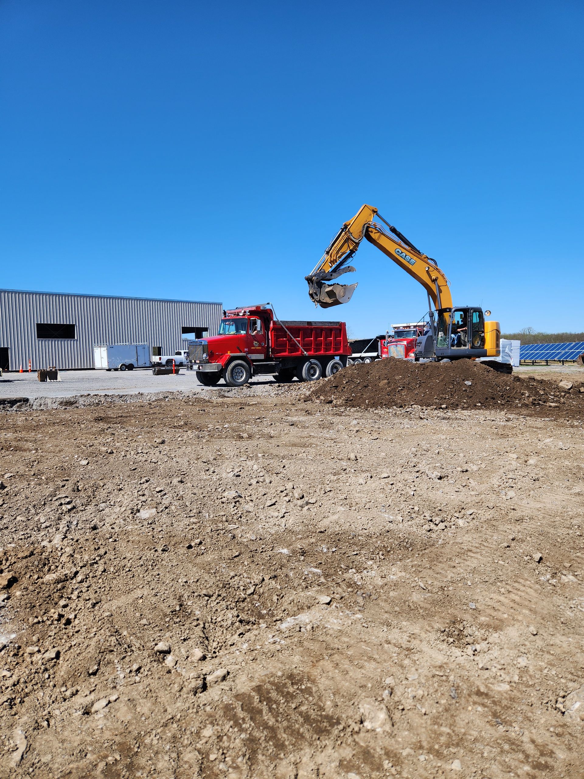 Construction site with excavator loading a red dump truck on dirt under a blue sky