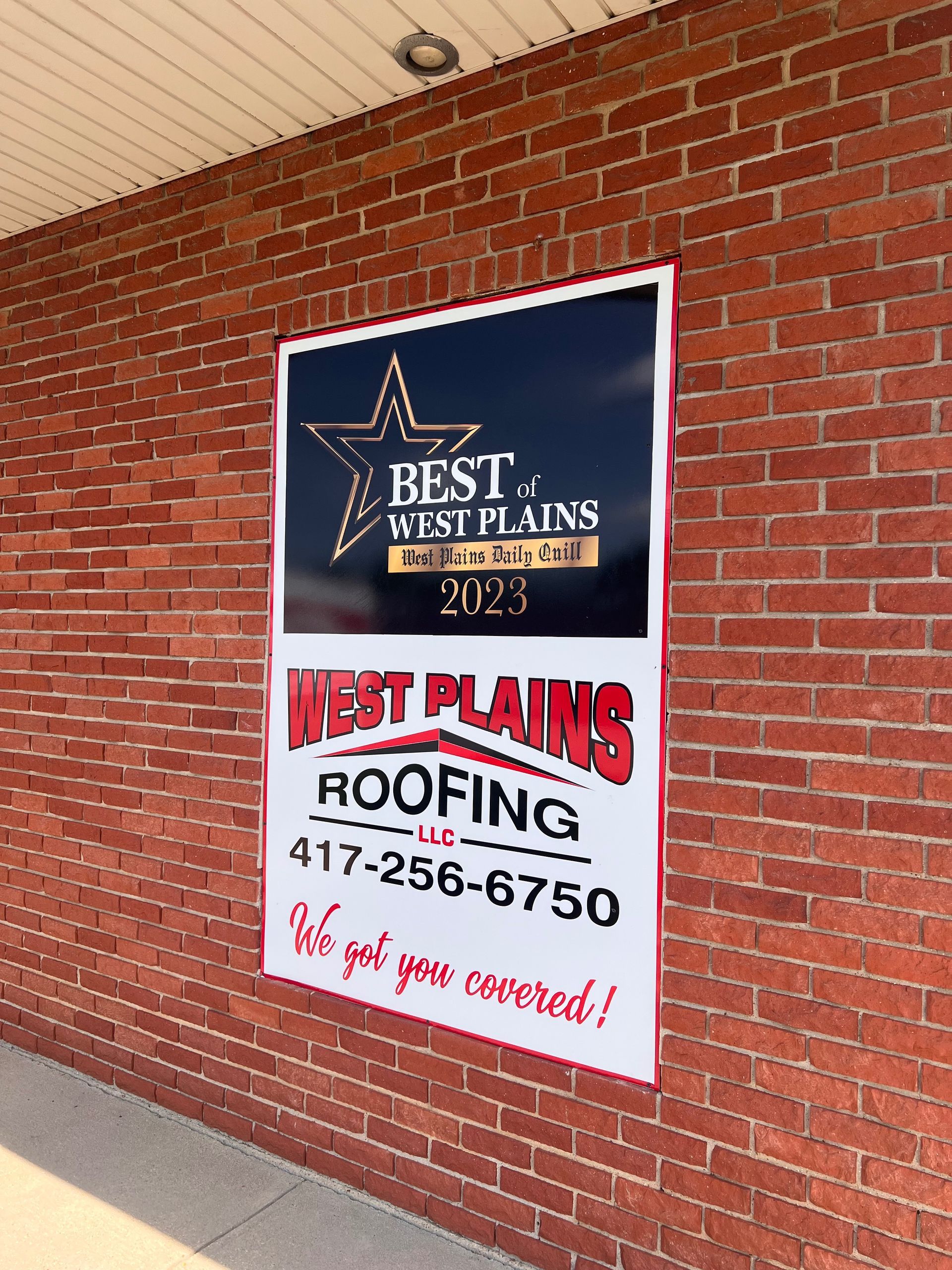 Sign for West Plains Roofing LLC on a brick wall. It announces their award as 