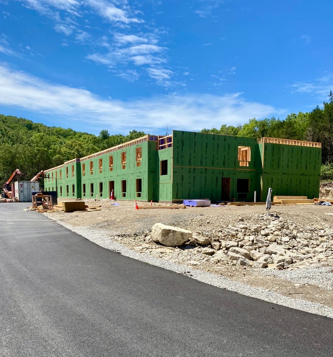 Building under construction, wood frame, green sheathing. Asphalt road, blue sky.