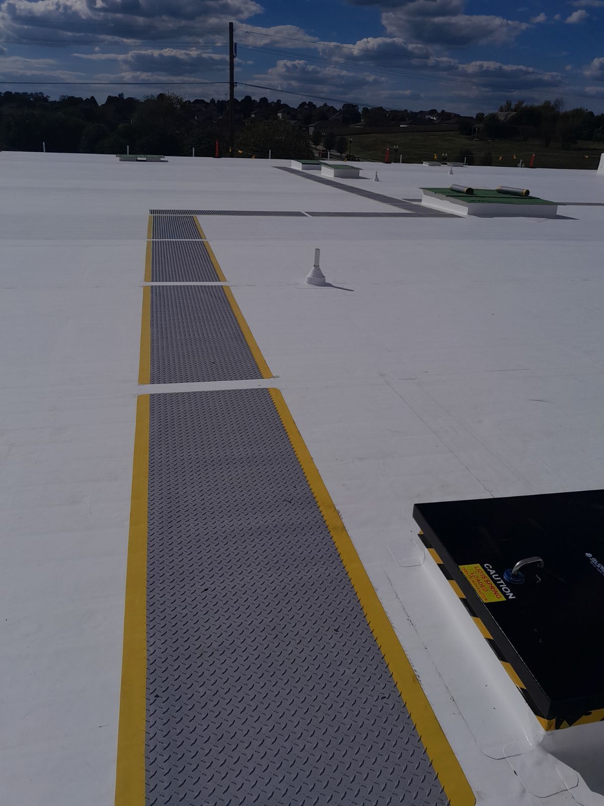 White roofing with a white angled edge. Construction materials and a field in the background under a cloudy sky.