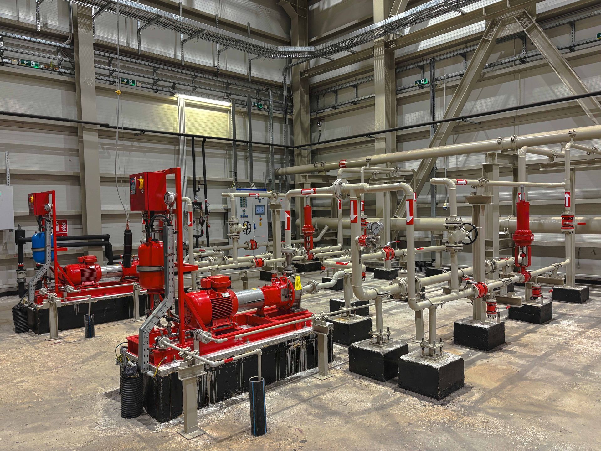 Industrial machinery with red pumps and silver pipes in a large room.