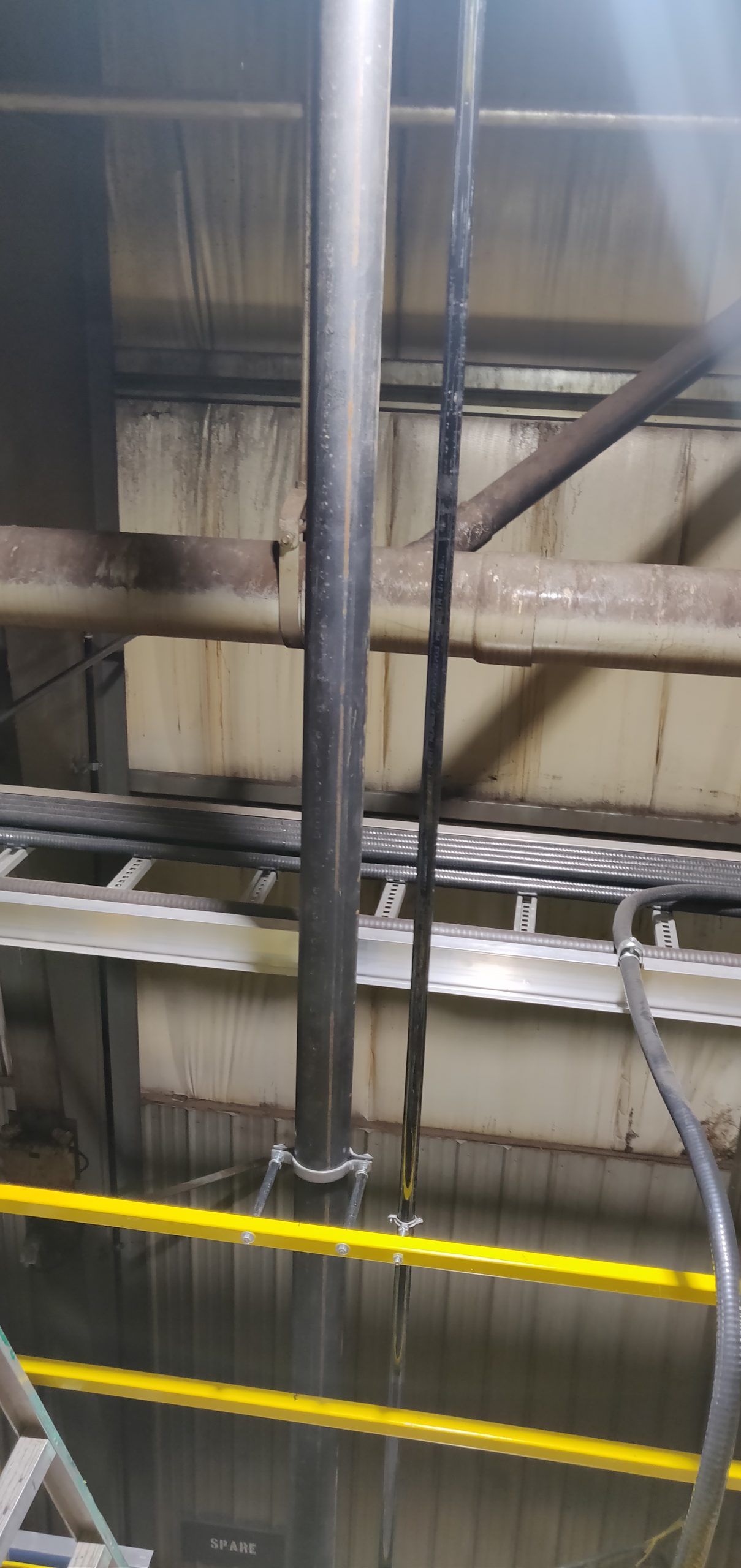 Pipes and cables in industrial setting, yellow railings in foreground.