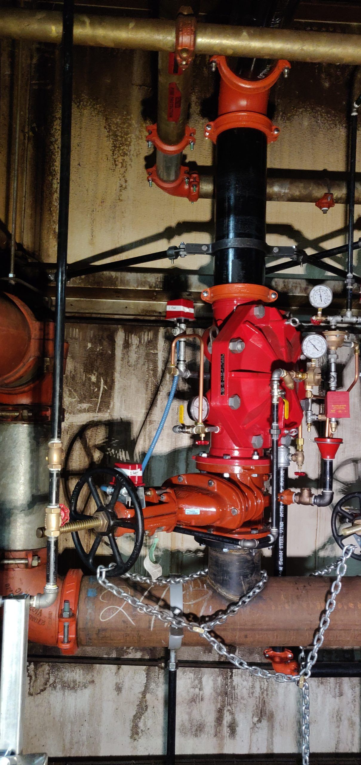 Red fire pump with pipes and gauges in an industrial setting.