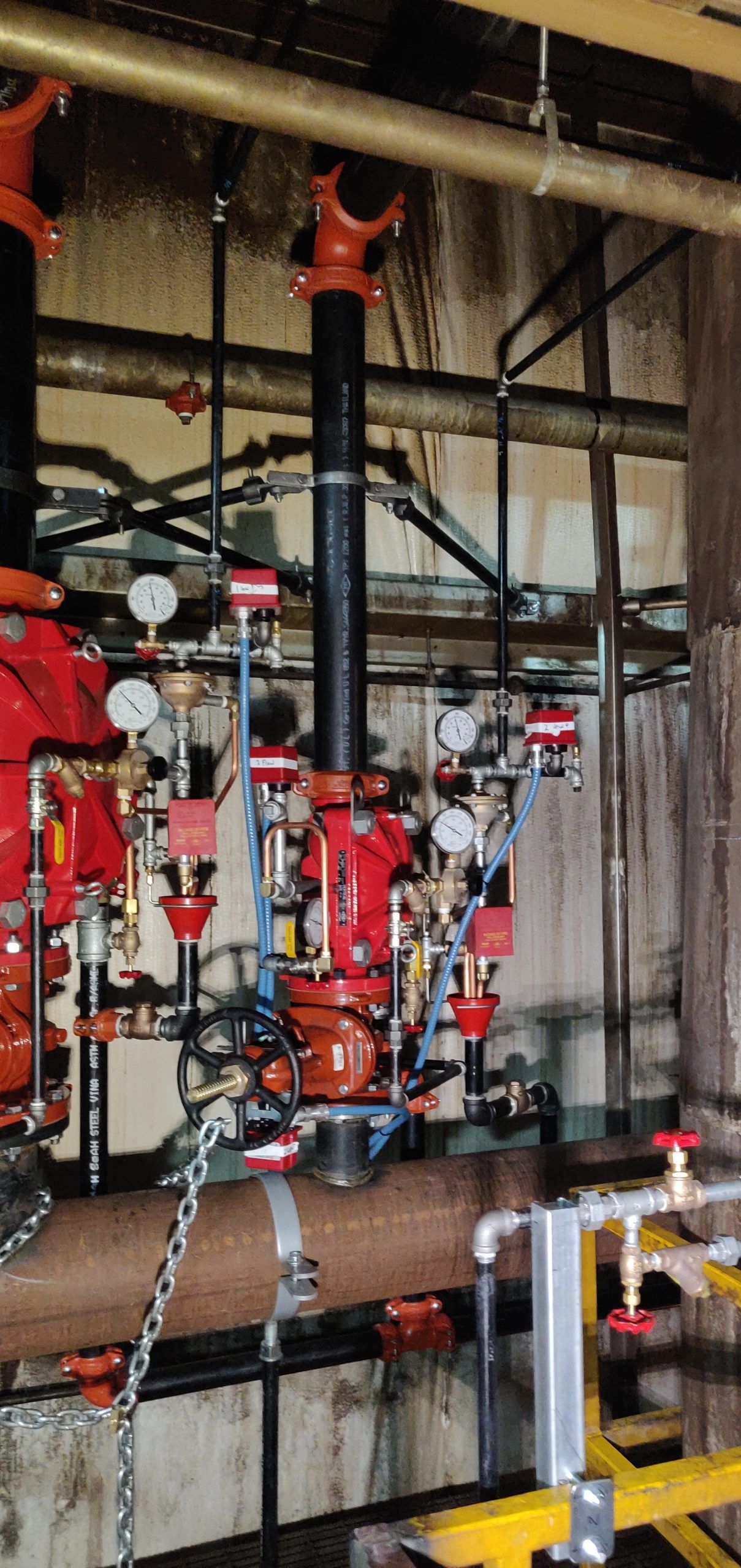 Complex fire suppression system with red valves, black pipes, and gauges in an industrial setting.