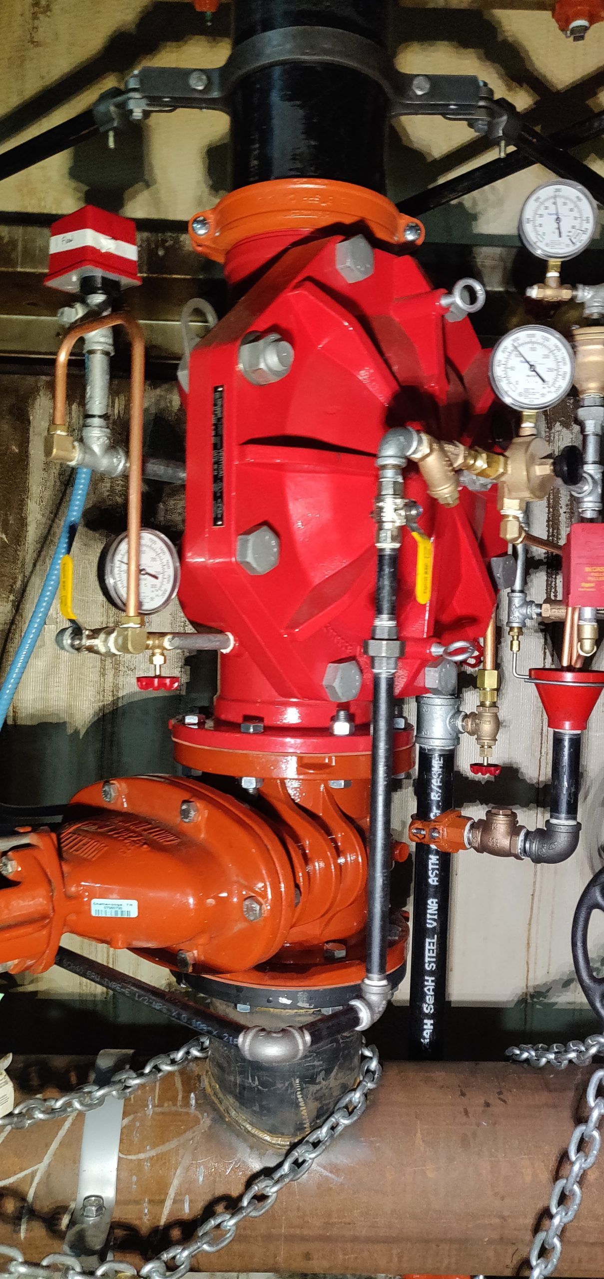 Red fire sprinkler control valve with gauges, piping, and chains.