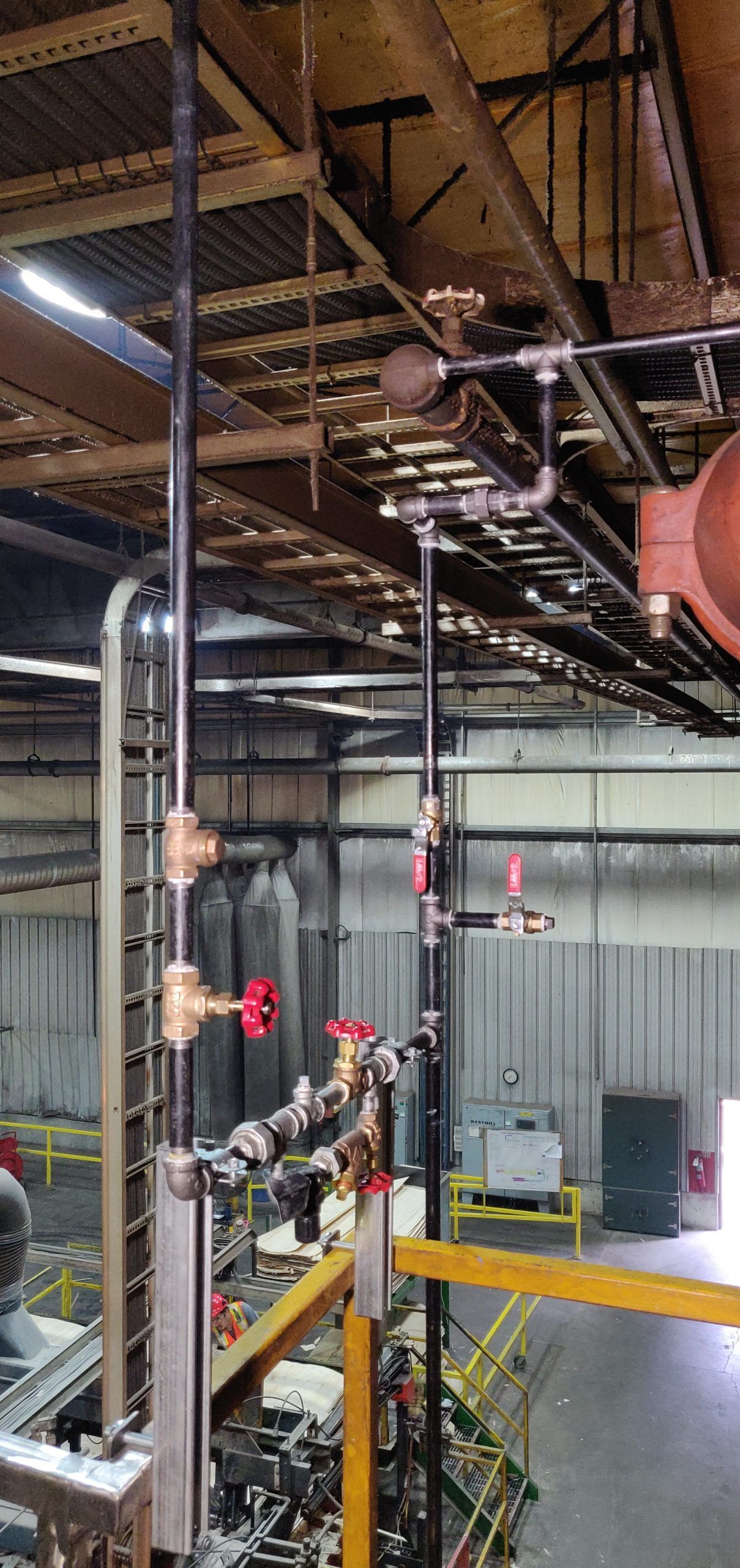 Pipes with valves and red handles run from the ceiling in an industrial setting, viewed from above.