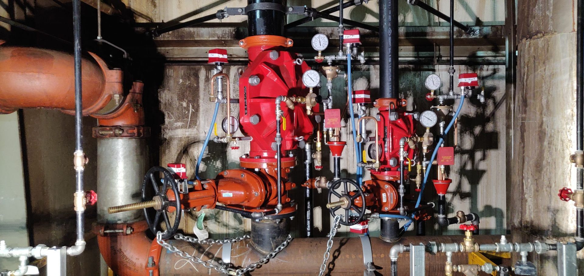 Red fire suppression system components with pipes, gauges, and valves in an industrial setting.