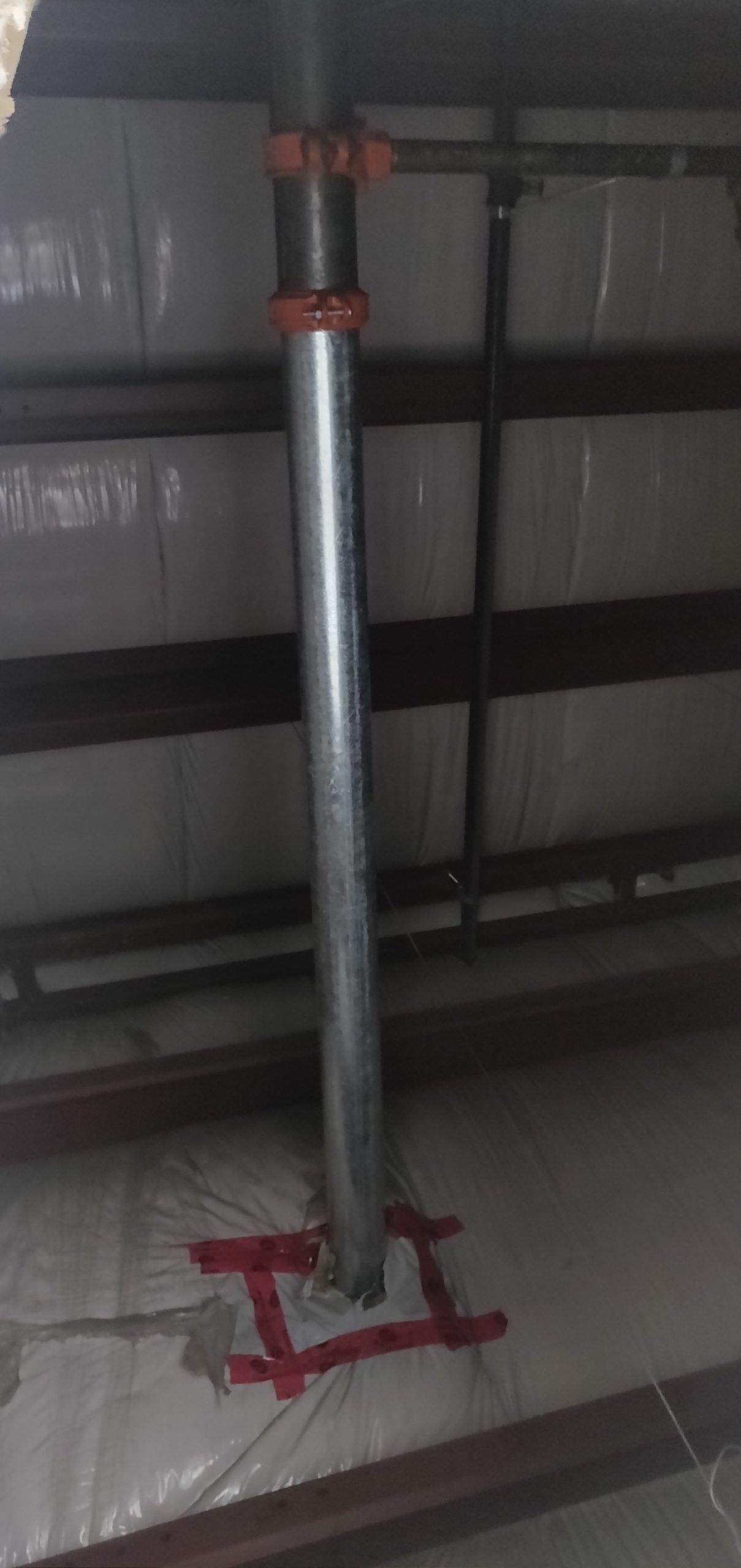 A silver pipe with red fittings secured to a ceiling with a red bracket.